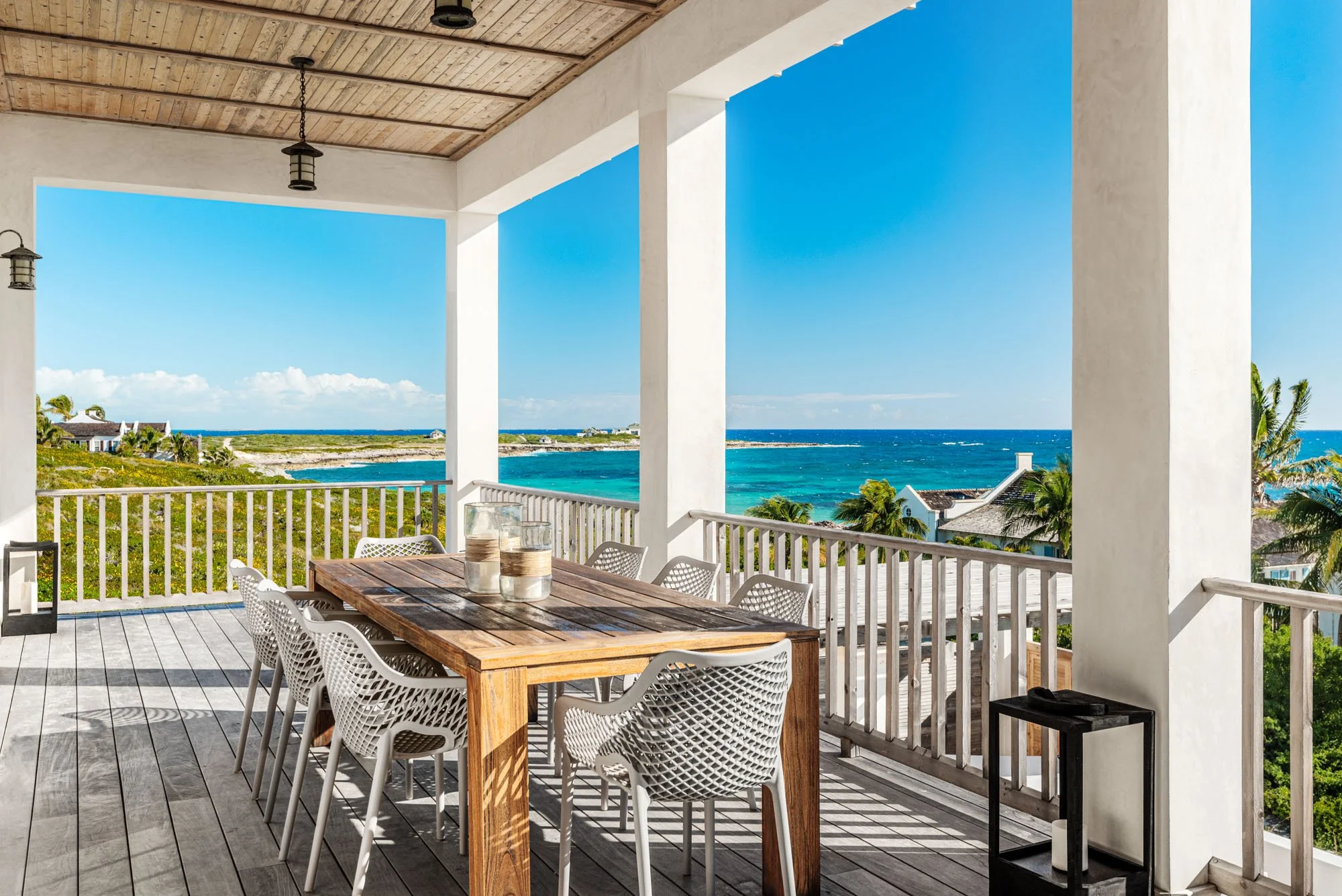 Covered outdoor dining deck at an Ambergris Cay villa in Turks and Caicos, with a teak table for eight, lanterns, and open views over the coastline and ocean