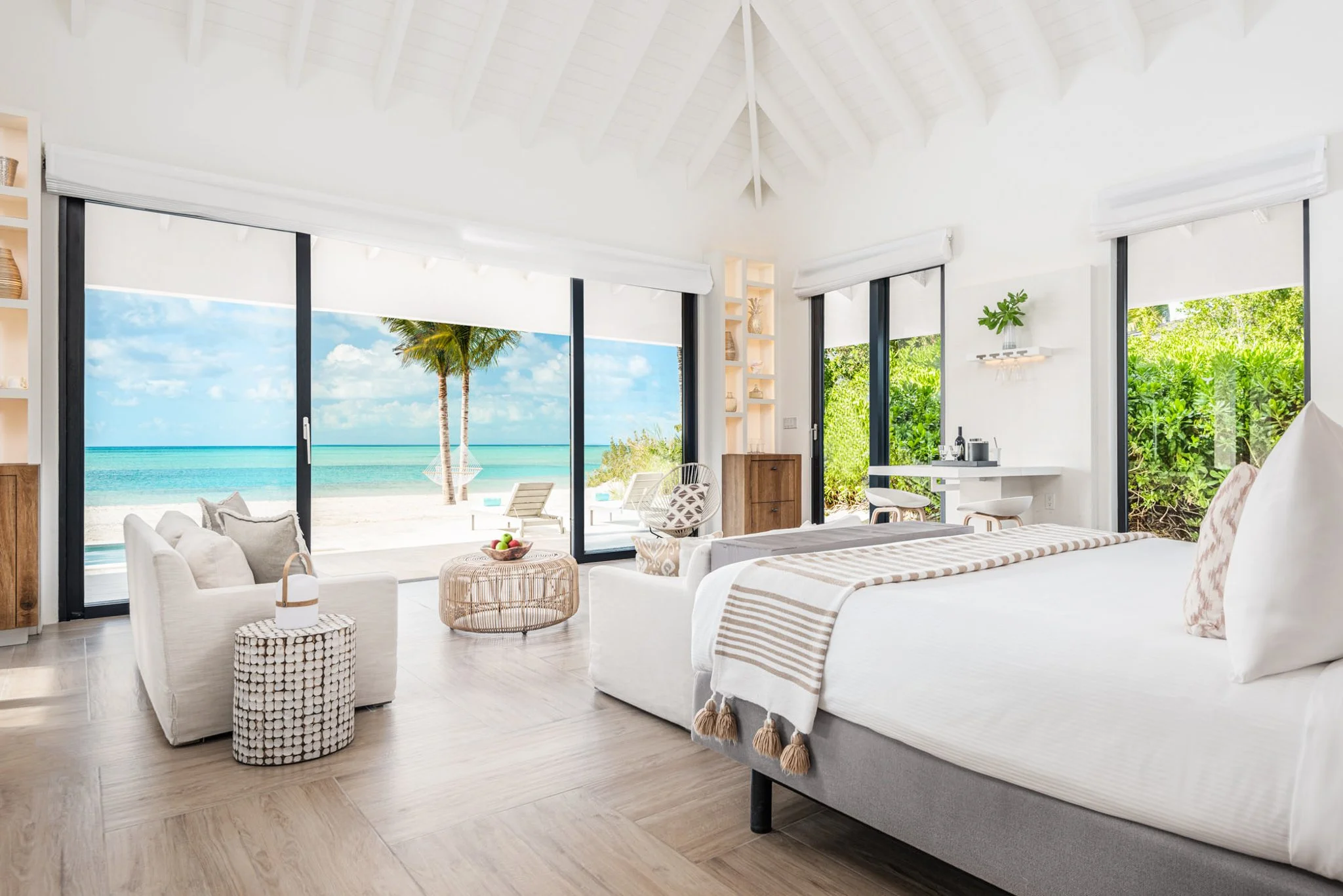 Interior of a Beachfront Bungalow at Ambergris Cay in Turks and Caicos, with a king bed, vaulted white ceiling, and sliding doors opening onto the sand and turquoise water