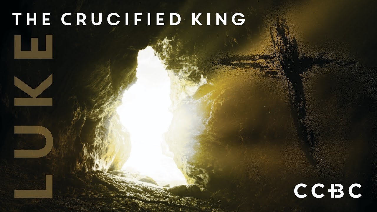 A dark cave with an opening illuminating a cross and light shining through, with the text 'The Crucified King' at the top and the words 'Luke' on the left and 'CCBC' on the bottom right.