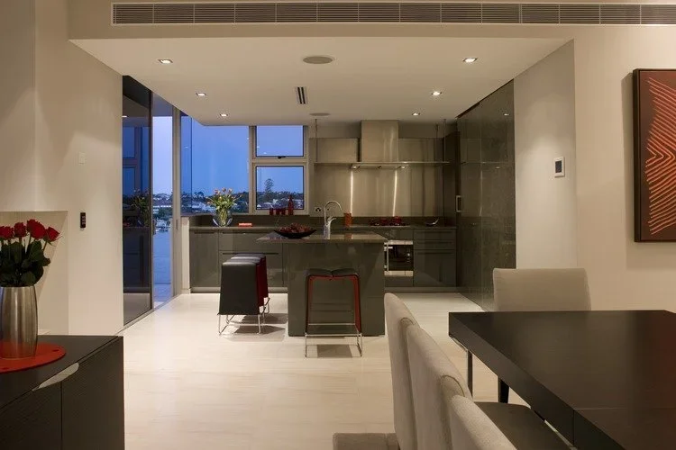 Modern kitchen with dark cabinets, island counter, stainless steel appliances, and large windows overlooking the outside.