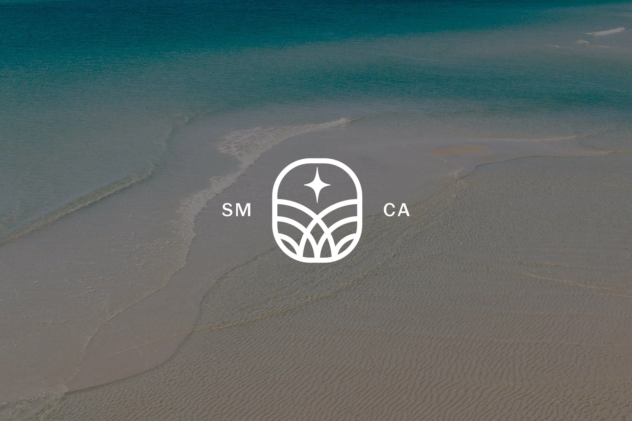 A beach with sand and ocean waves, featuring a white icon in the center with the letters 'SM' on the left, 'CA' on the right, and a star above a stylized landscape design.