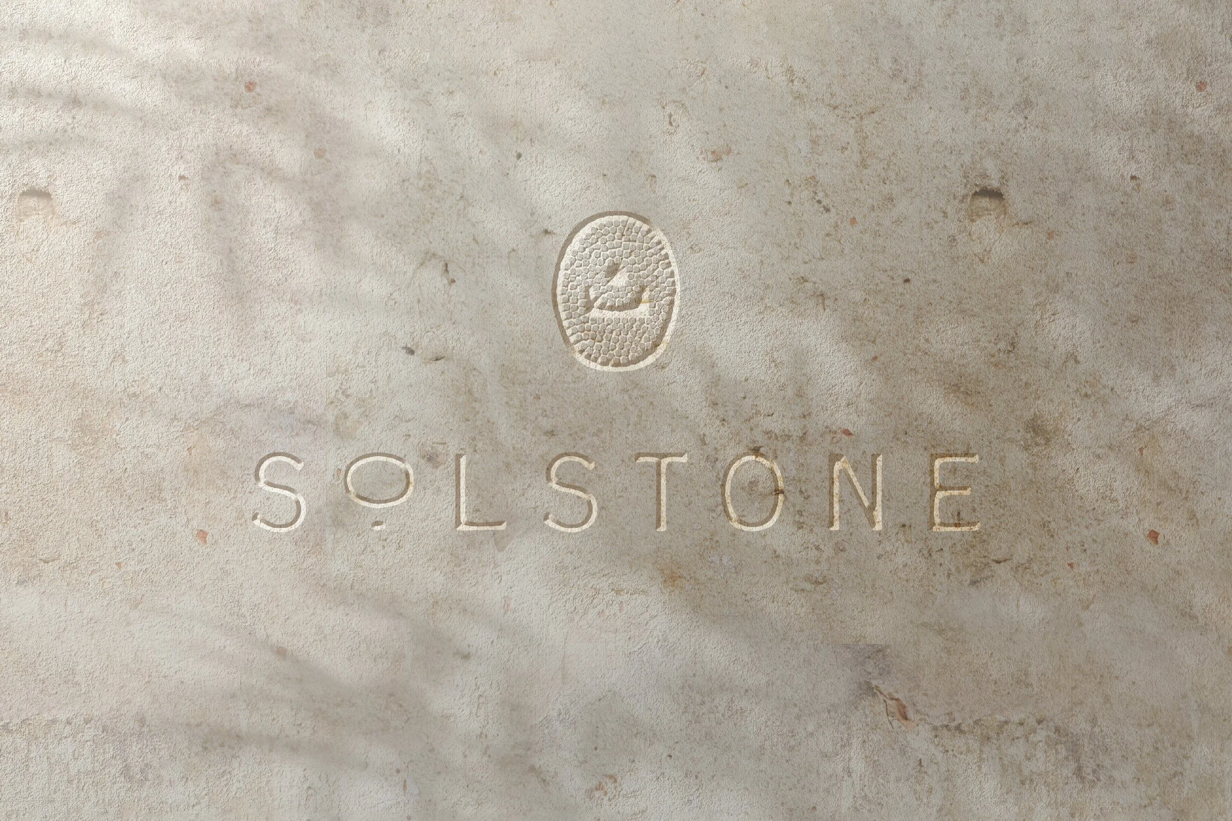 Close-up of a pale beige stone surface with ‘SOLSTONE’ etched into it and a small embossed icon above, showing a stylized marble or stone within a textured oval.
