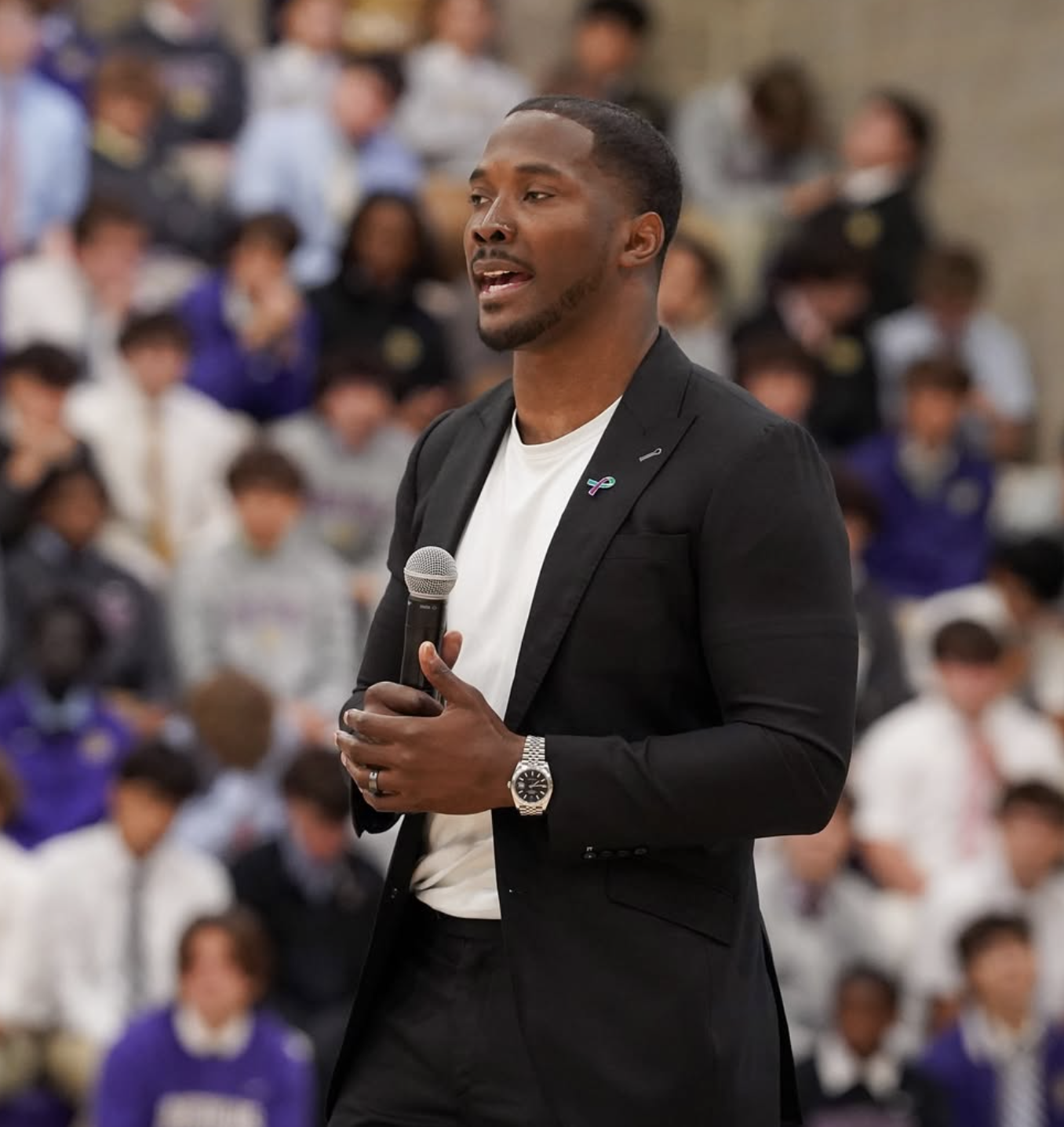 A man speaking into a microphone during a presentation or speech in a crowded indoor setting.