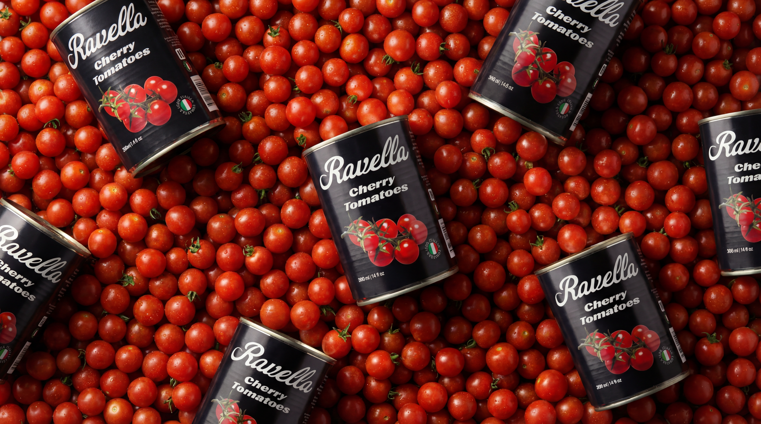 Multiple cans of Ravella cherry tomatoes placed on a bed of fresh cherry tomatoes.