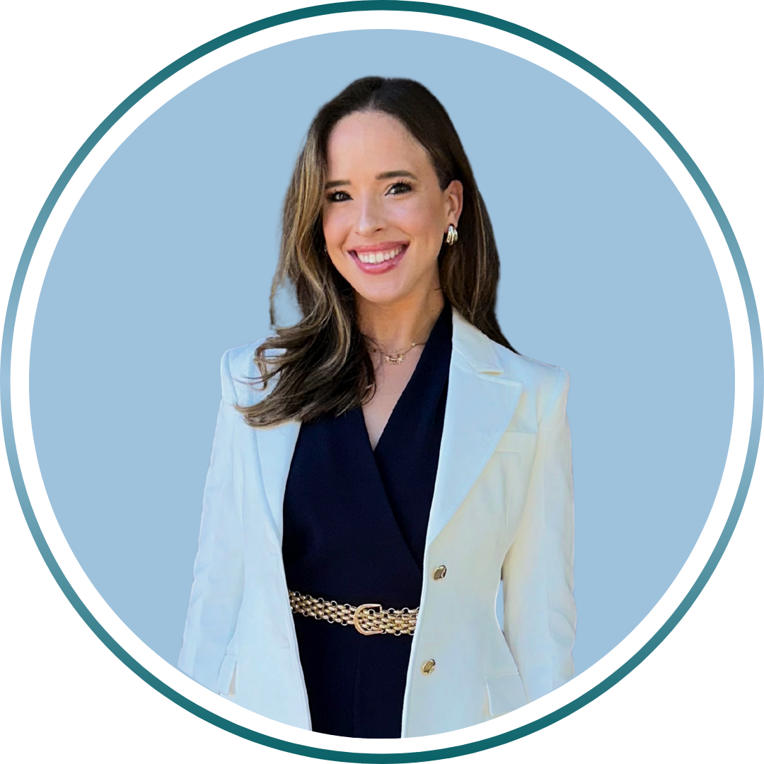 A smiling woman with long brown hair, dressed in a white blazer and black top, standing against a light blue background.