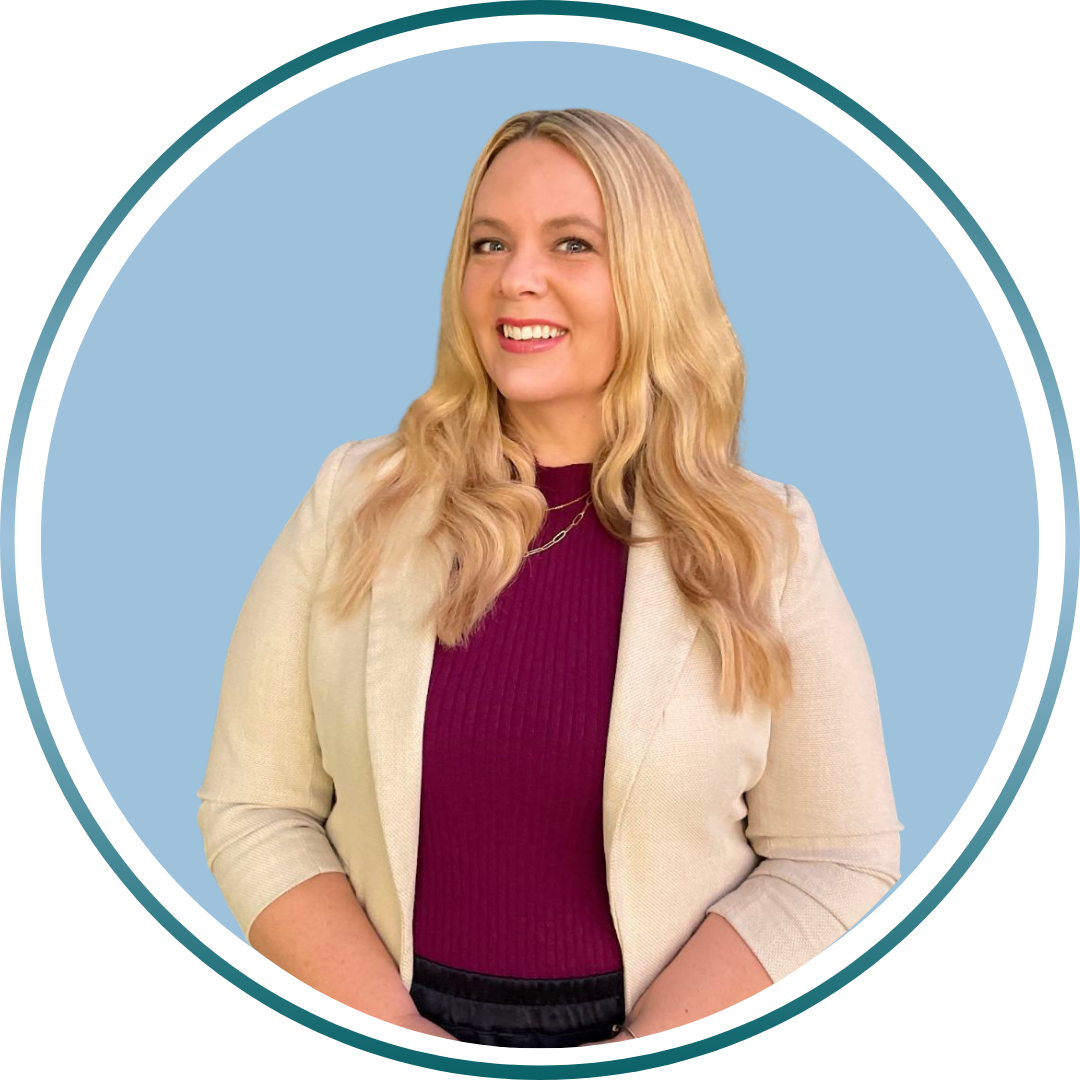 A woman with blonde hair wearing a white blazer and a maroon top, smiling against a light blue background.