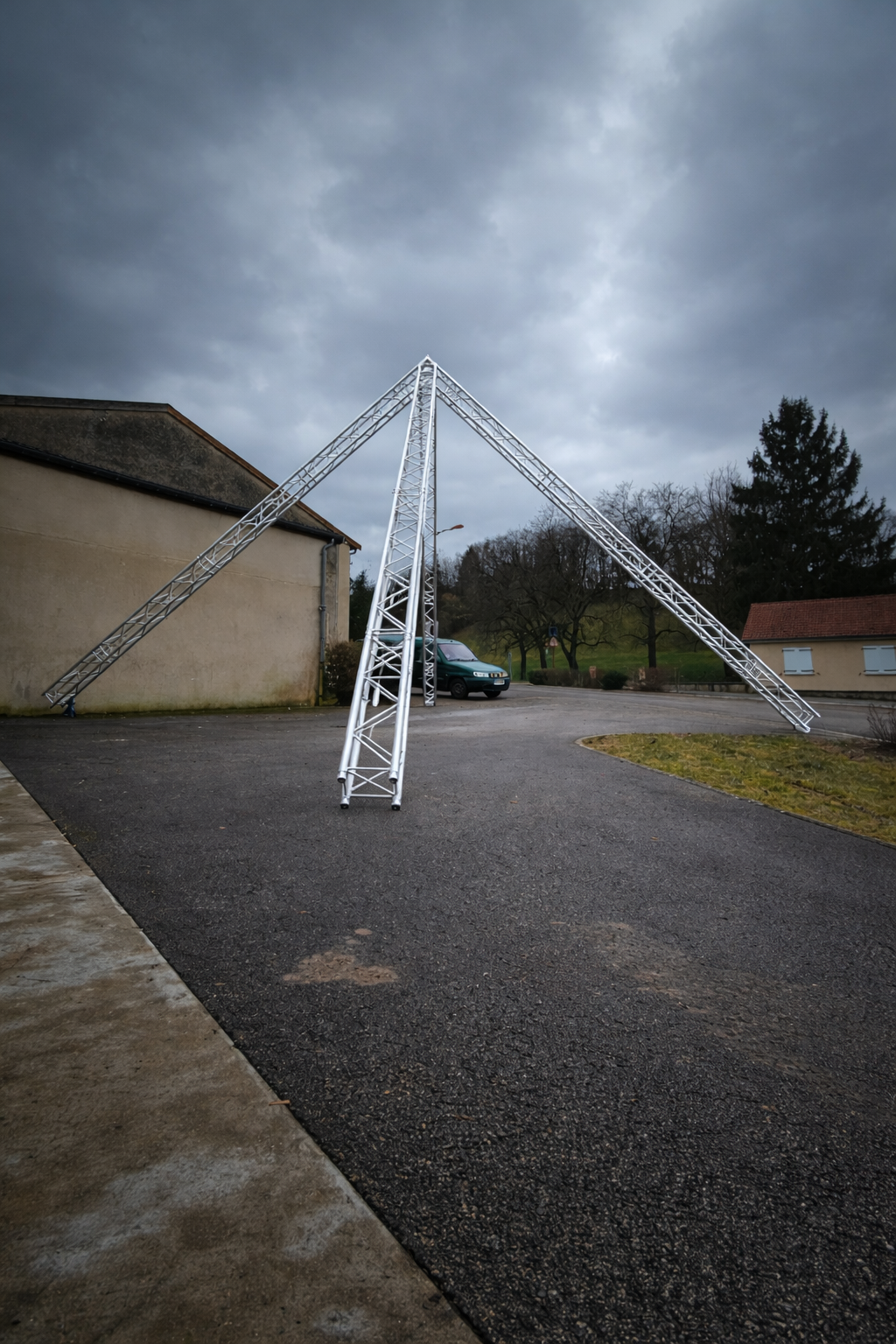 Structure métallique en forme de pyramide sur une surface asphaltée, ciel nuageux en arrière-plan.