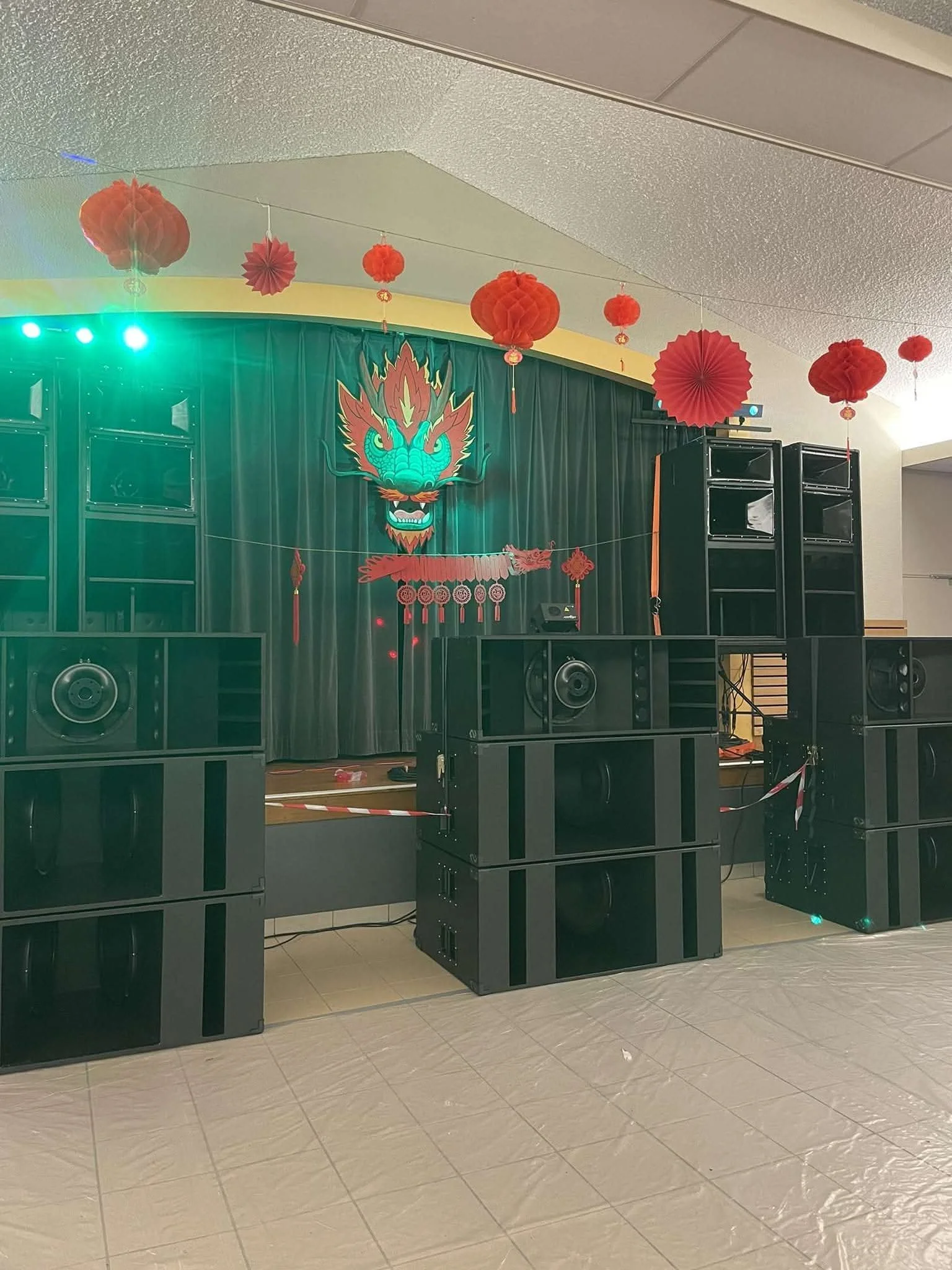 Installation sonore avec plusieurs haut-parleurs sur le sol, décorations porcelaine rouges suspendues au plafond, et un rideau vert avec un dessin de dragon chinois en arrière-plan, indiquant une célébration culturelle ou un événement festif.