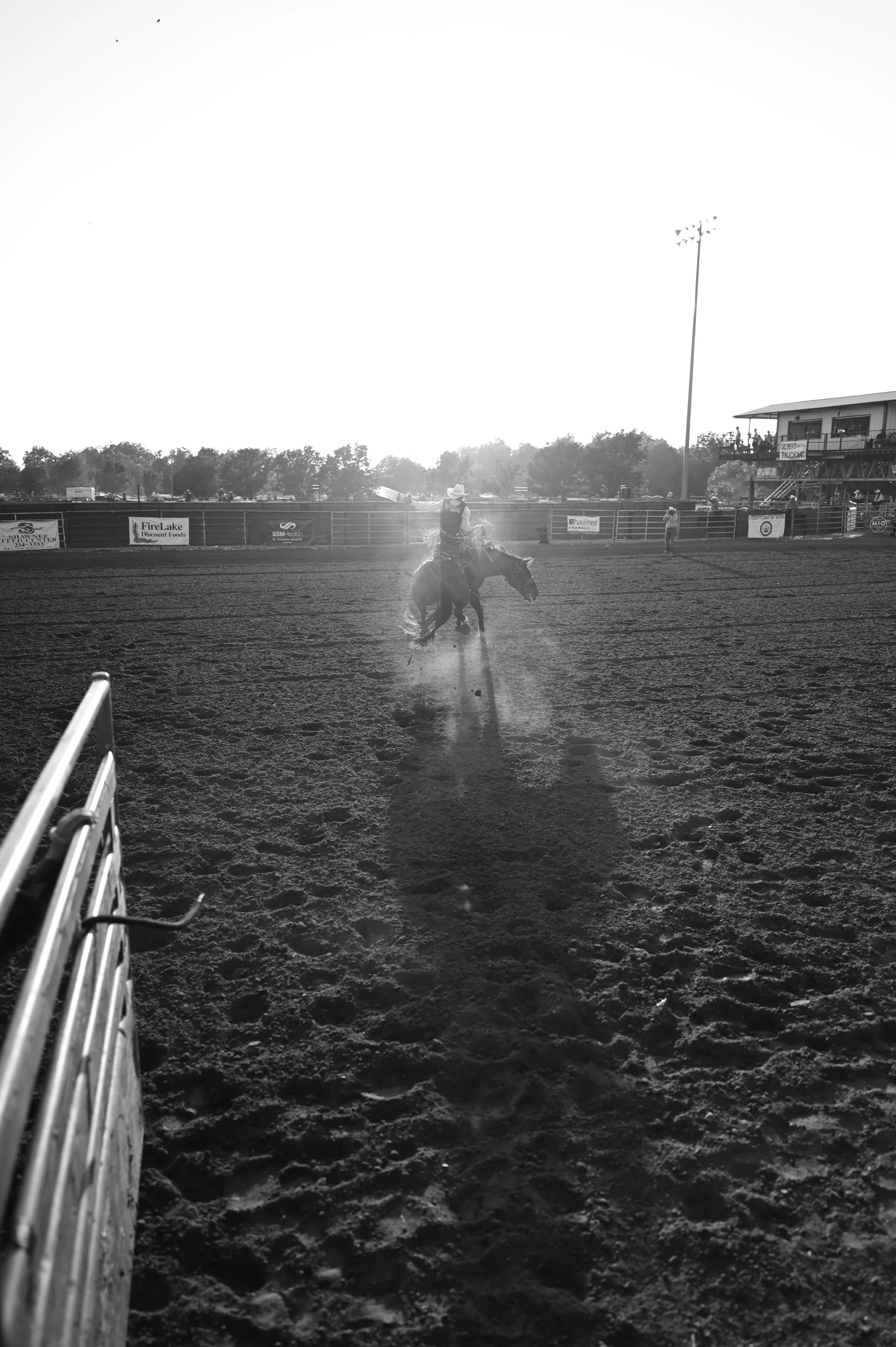 A cowboy riding a horse on a dirt rodeo arena at sunset.