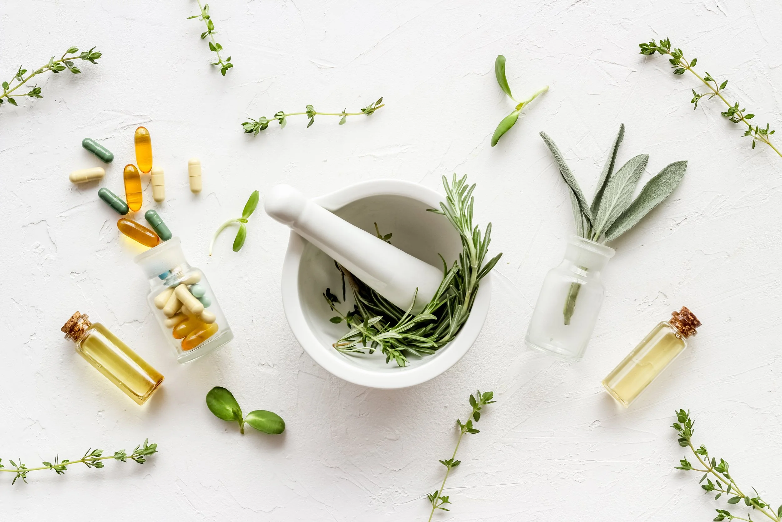 Herbs and essential oils with capsules and pills on a white surface.