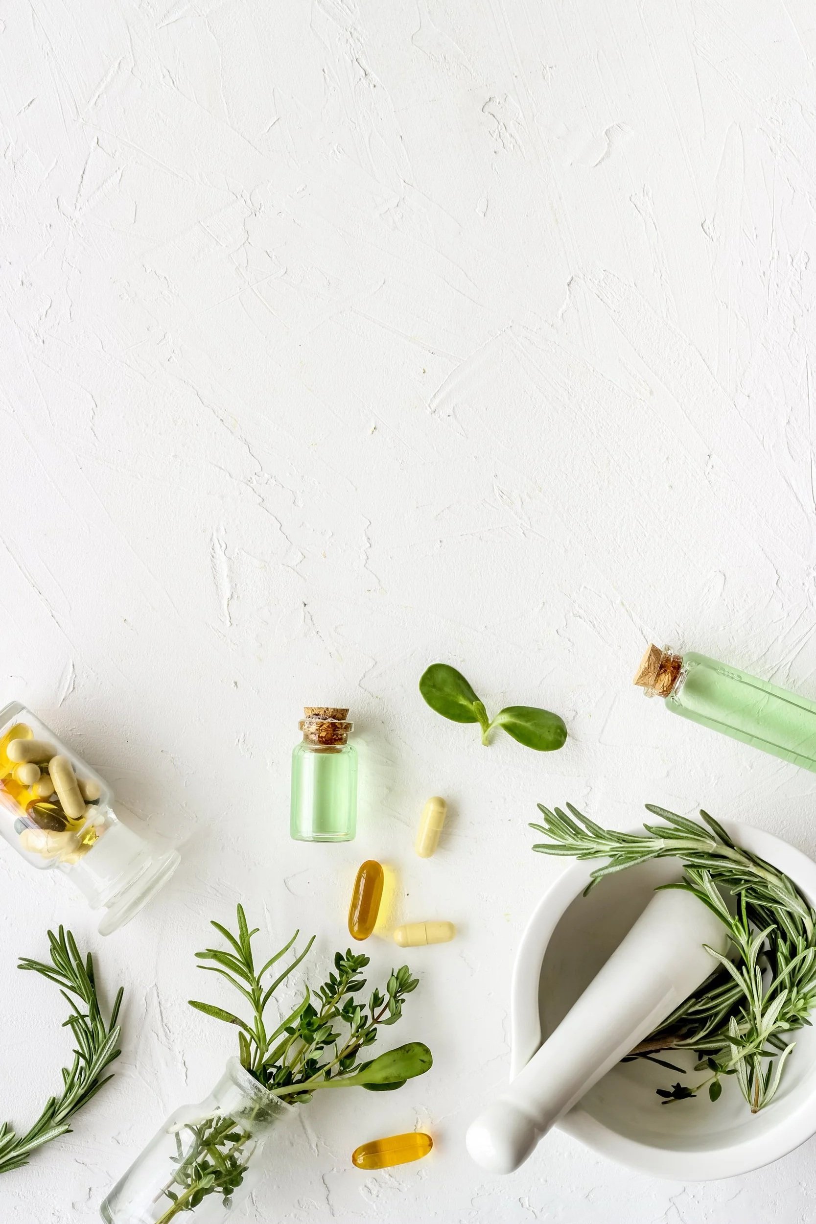 Herbs, capsules, and small bottles on a white textured surface, with a mortar and pestle filled with herbs.