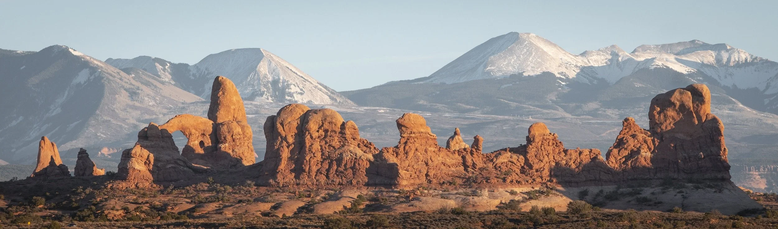 Rock formations in the foreground with snow-capped mountains in the background under a clear sky.