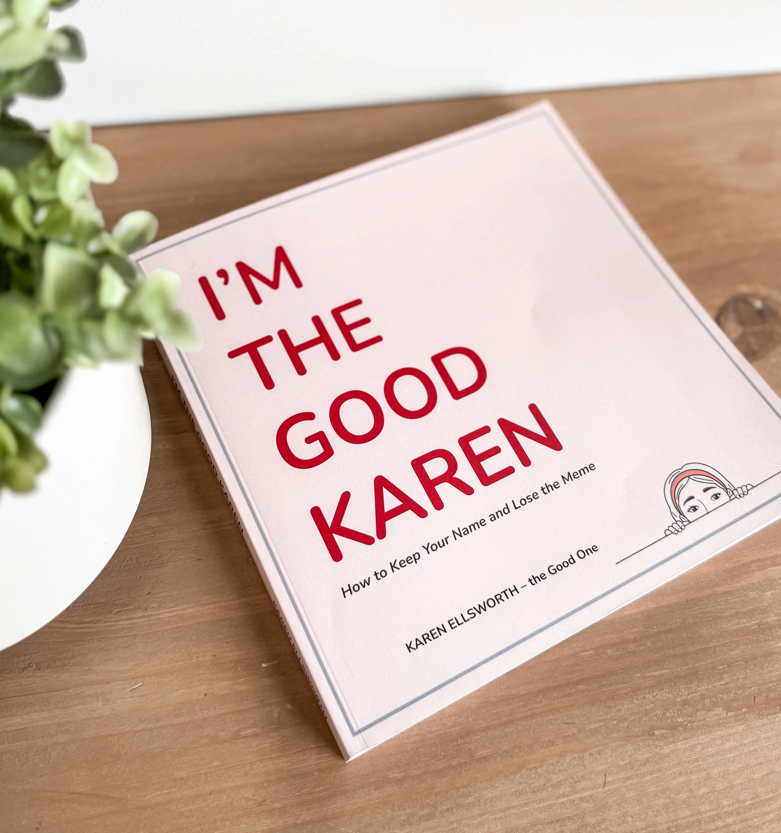 Book titled 'I'm the Good Karen' on a wooden table next to a potted plant.