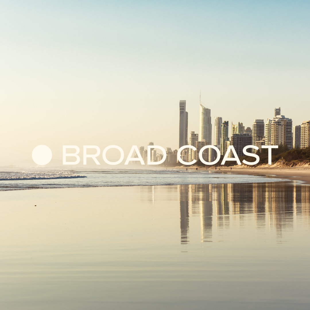 A beach with a city skyline in the background, reflecting on the wet sand, during daytime.