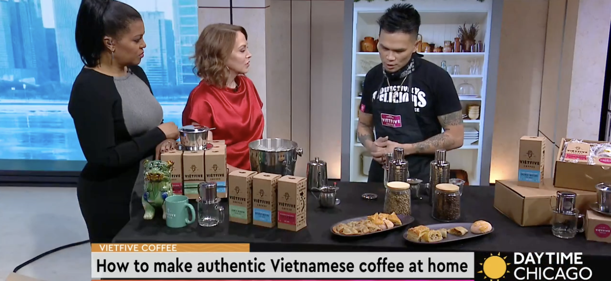 Television segment on how to make authentic Vietnamese coffee, with three women and a man, various coffee ingredients, and snacks on the table.