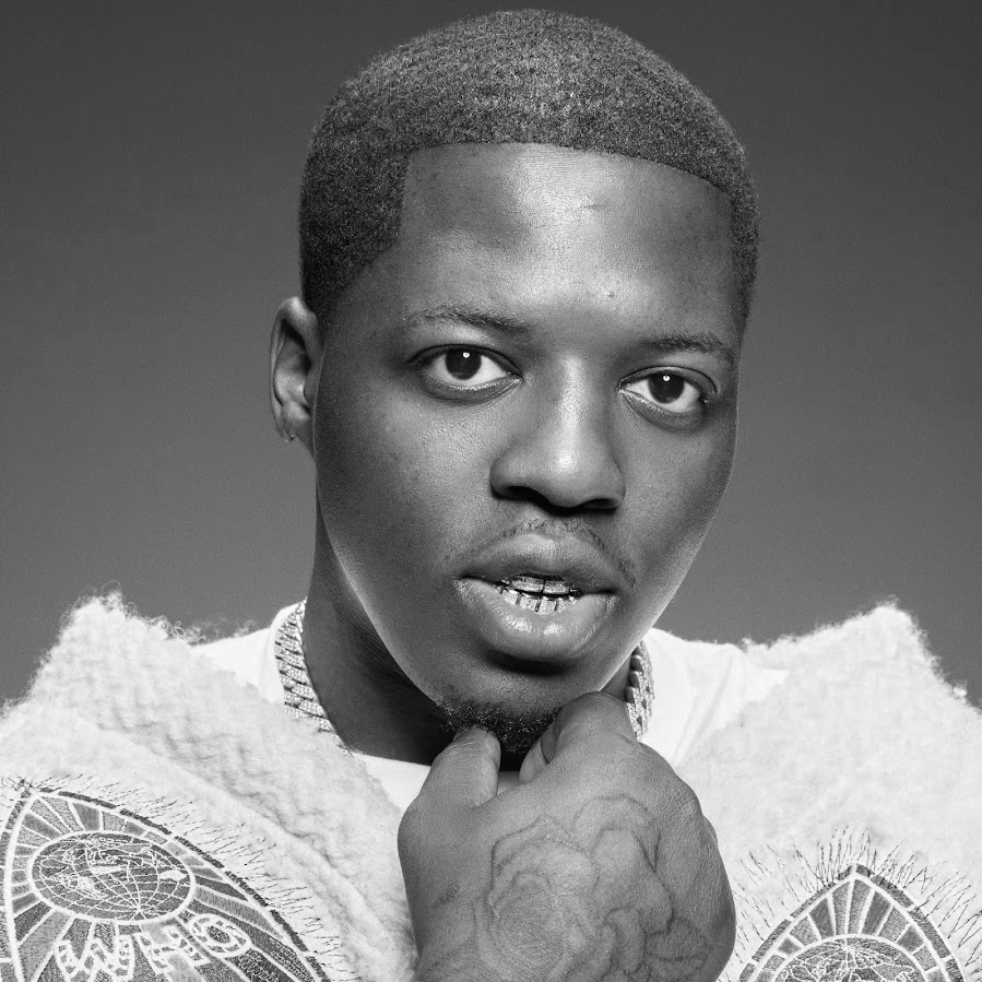 Black and white portrait of a young man with short hair, looking directly at the camera with his hand resting under his chin.