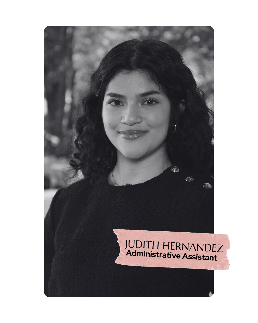 Black-and-white portrait of Judith Hernandez, smiling with curly hair, wearing a black sweater with decorative buttons, and a pink label with her name and title 'Administrative Assistant' at the bottom.