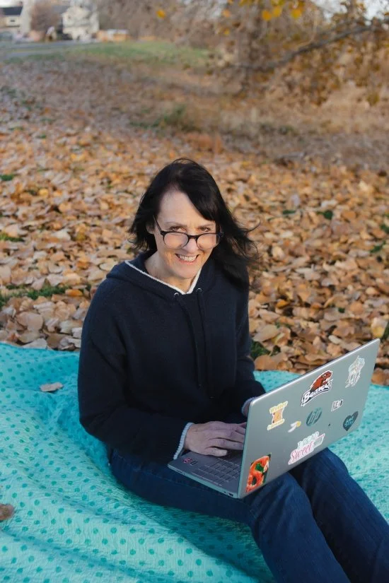 Clearsite Designer Alison peeps over the top of her reading glasses as she sits on a blanket in fall leaves with her computer on her lap