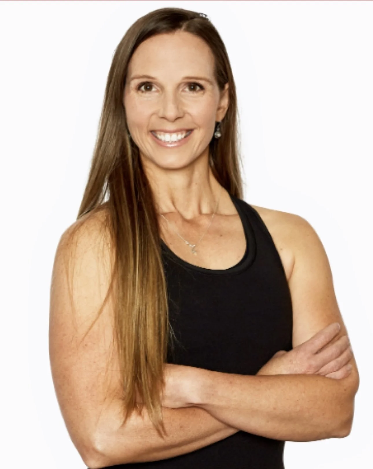 A woman with long brown hair smiling, wearing a black sleeveless top, standing with arms crossed against a white background.