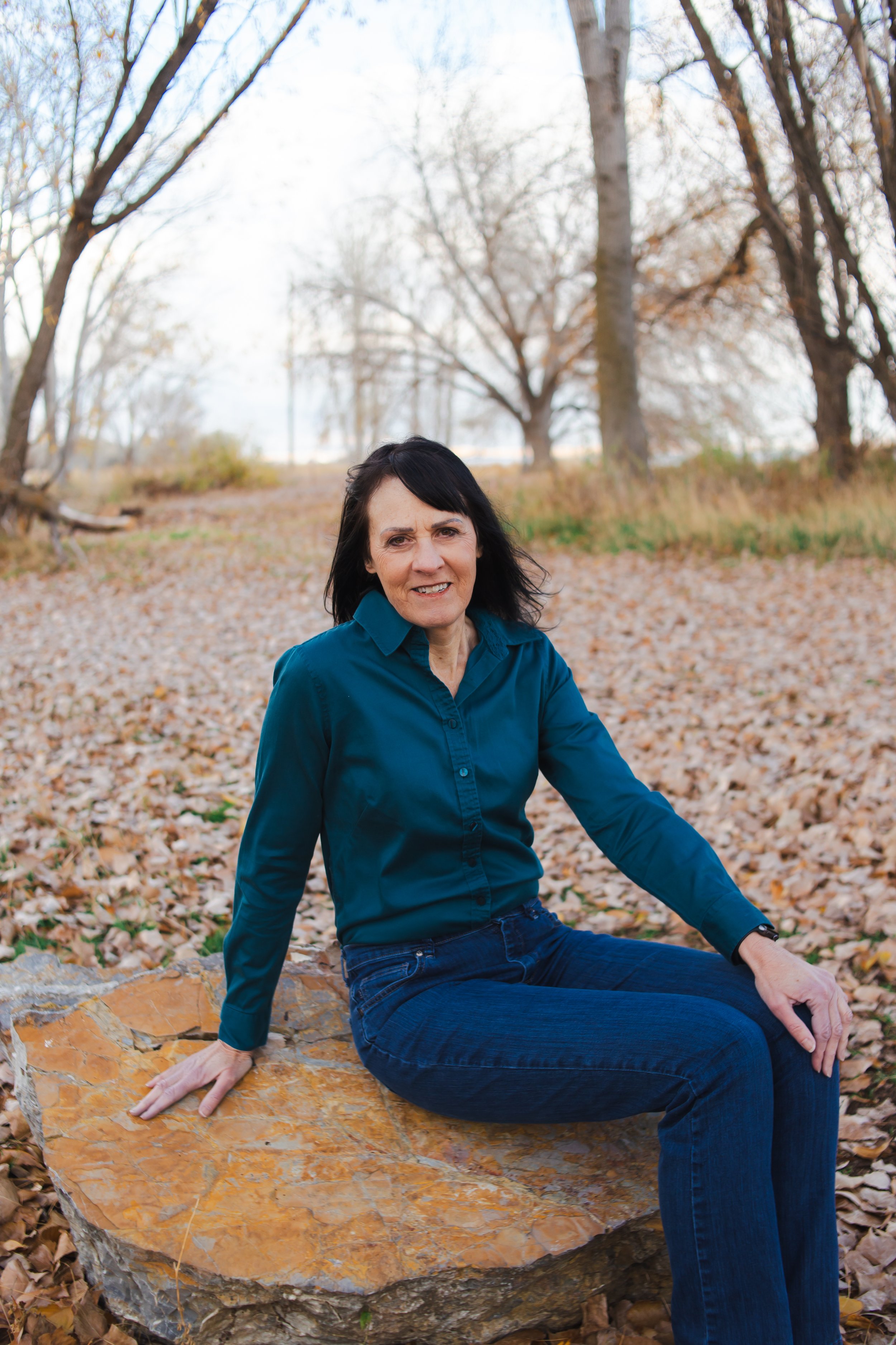 ClearSite Designer Alison sits on a rock and is surrounded by fall leaves. A lake is seen in the background