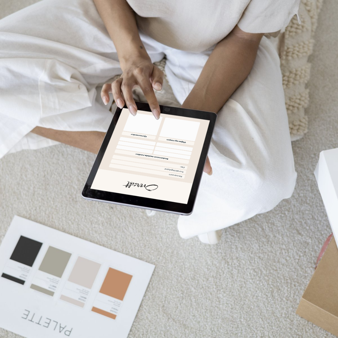 En person holder et nettbrett med en digital kontrakt som signeres, mens de er sittende på en hvit sofa. På gulvet foran dem ligger en fargeprøve-ark.