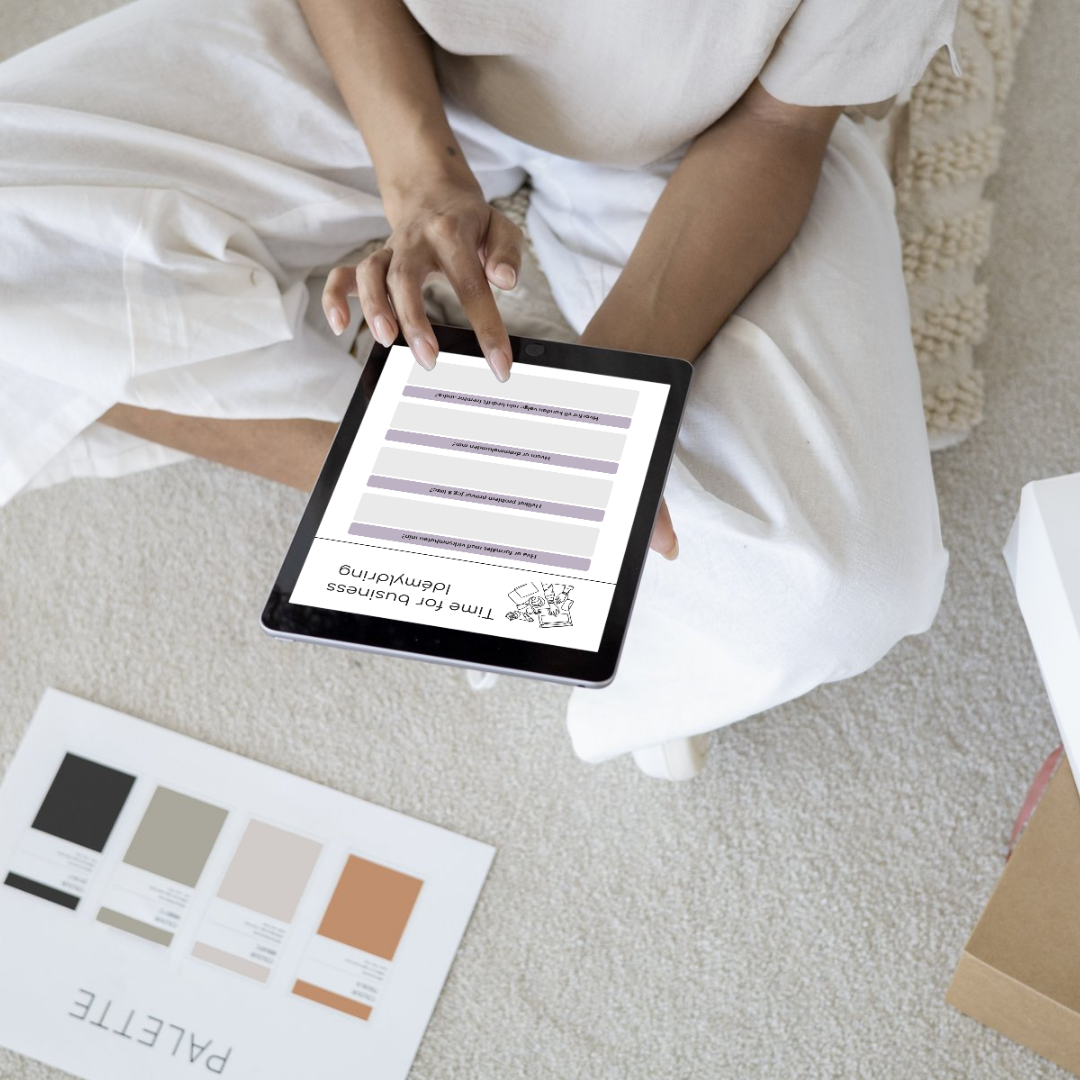En person sitter på gulvet med hvite klær, ser på et nettbrett med ett forretningsdokument. På gulvet foran ligger det fargeprøver,