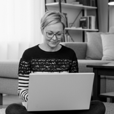 Kvinne med kort blond hår og briller som bruker en bærbar datamaskin i et hjemmekontor.