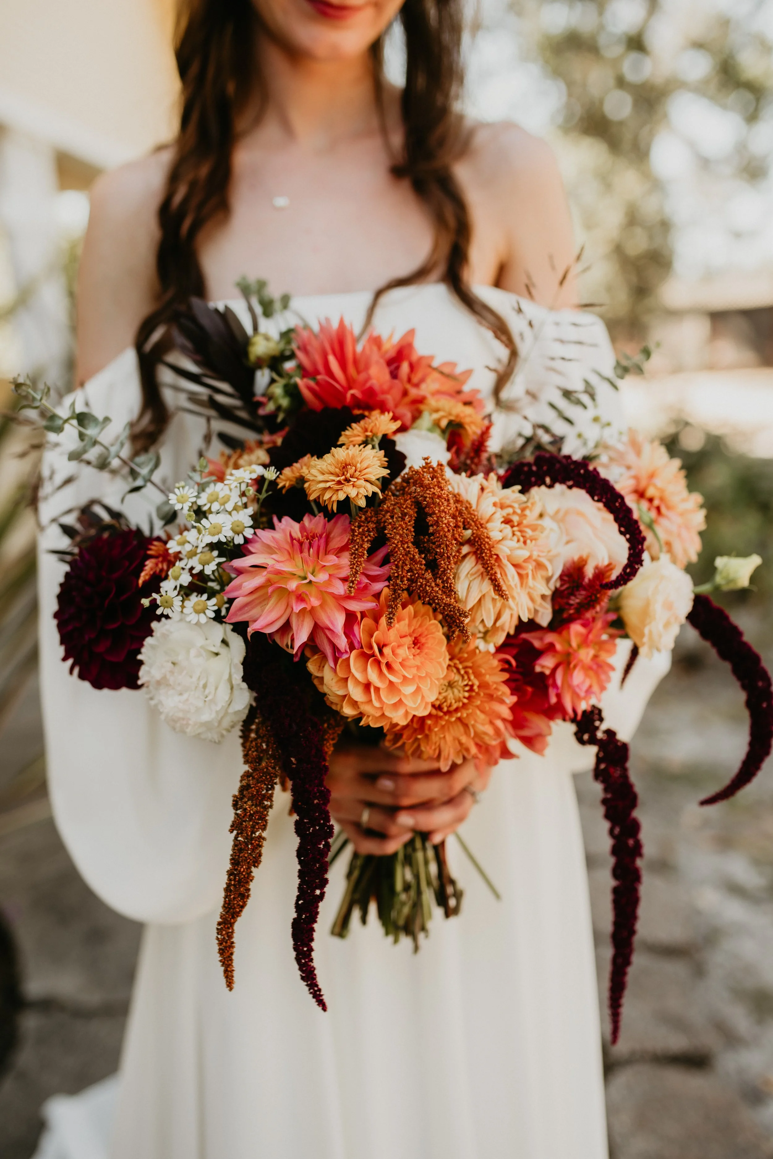 A woman in a white off-shoulder dress holding a large bouquet of colorful flowers.