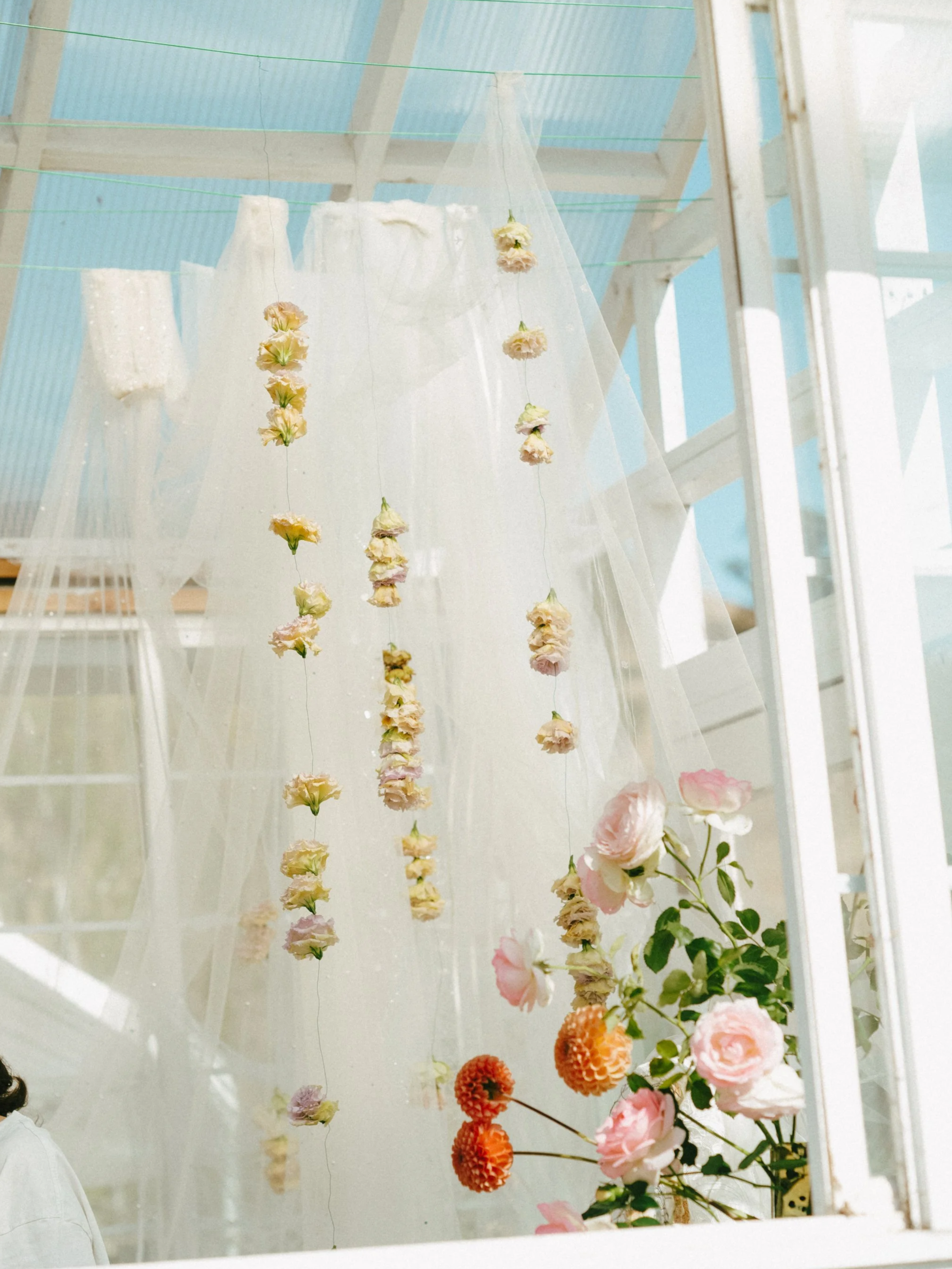 Decorative hanging flower garlands and a bouquet of pink and orange flowers inside a bright, airy space with white walls and a blue ceiling.