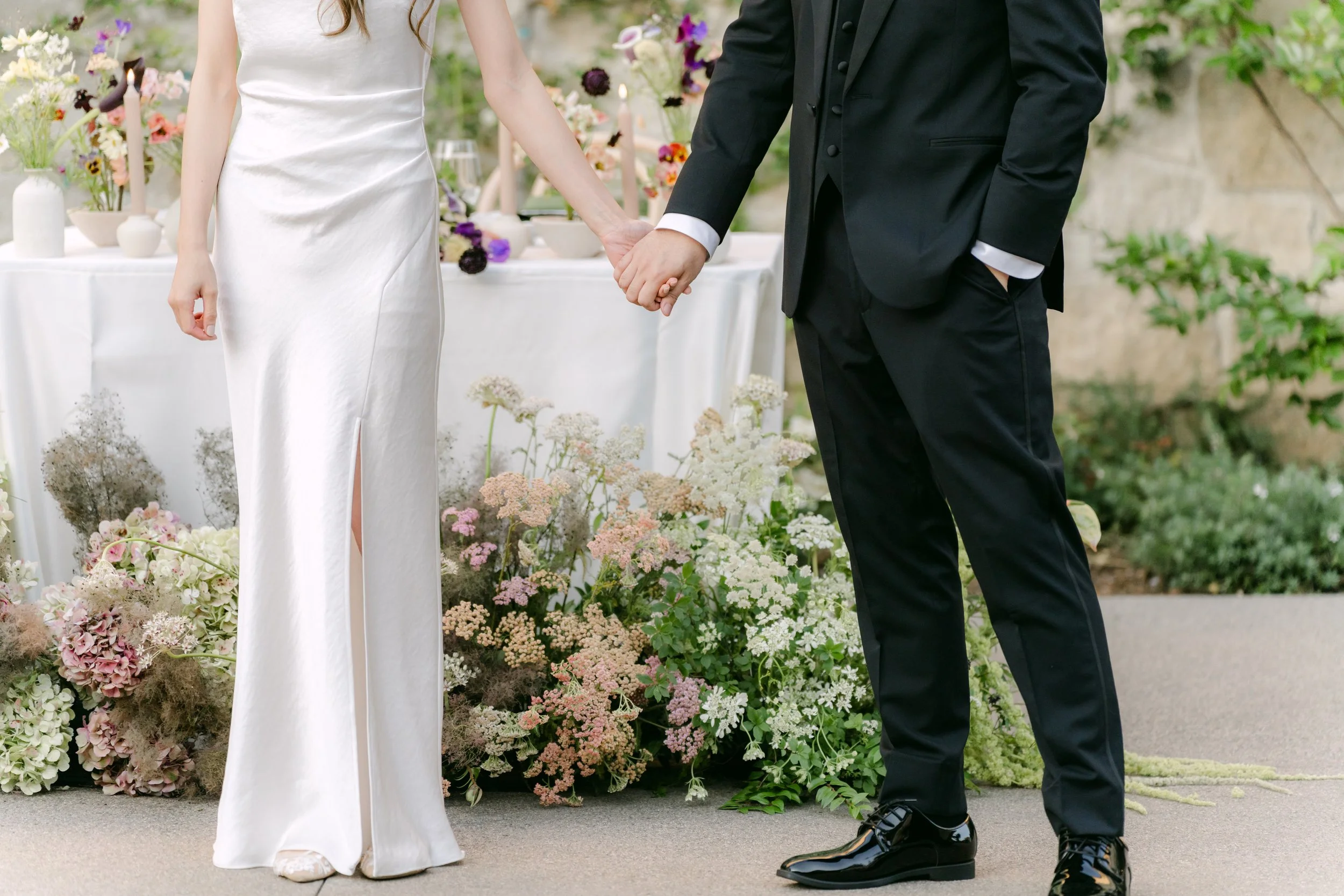 A bride and groom holding hands during their wedding ceremony, with flowers and a decorated table in the background.
