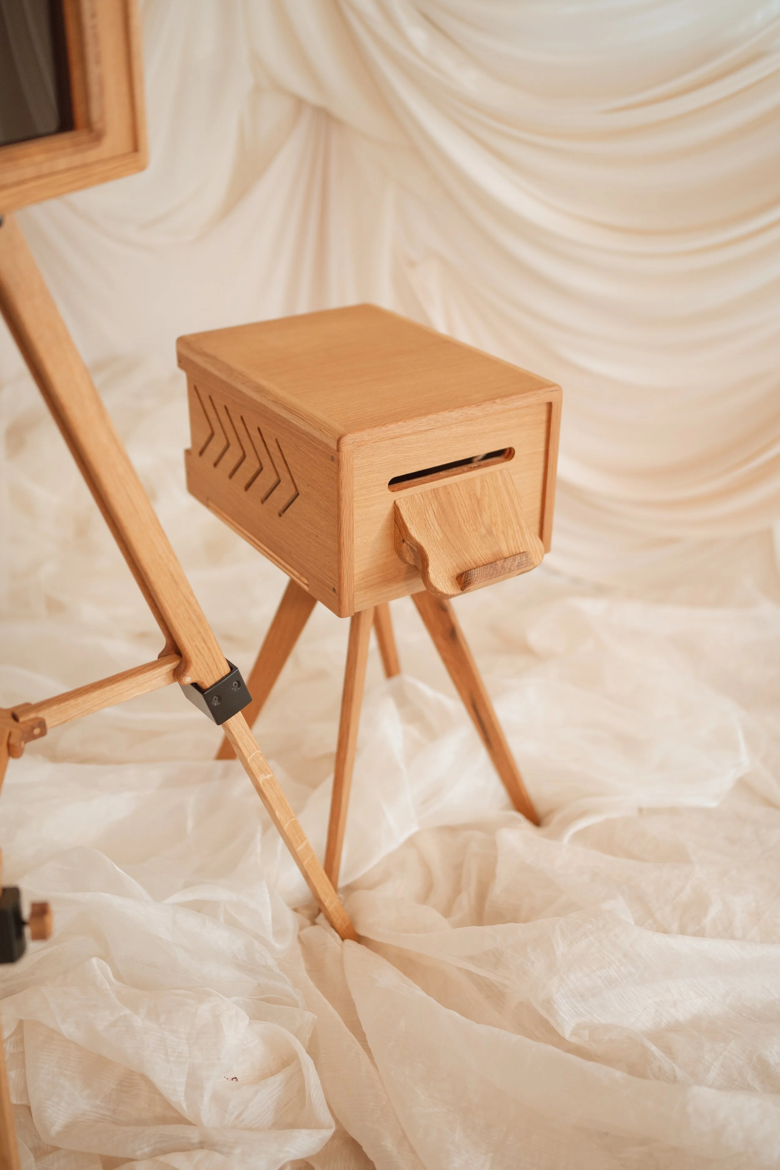 A wooden bee box on a stand with a carved entrance, set against a white draped fabric backdrop.