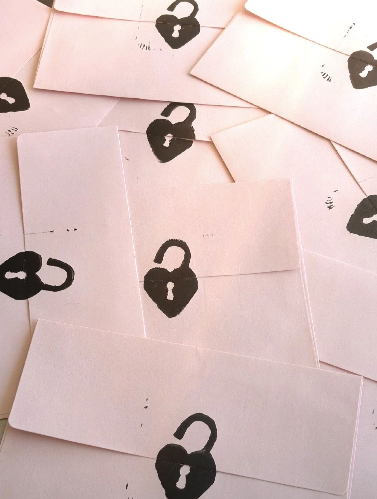 Multiple pink envelopes with black hand stamped heart shaped lock symbol printed on them, scattered on a surface.
