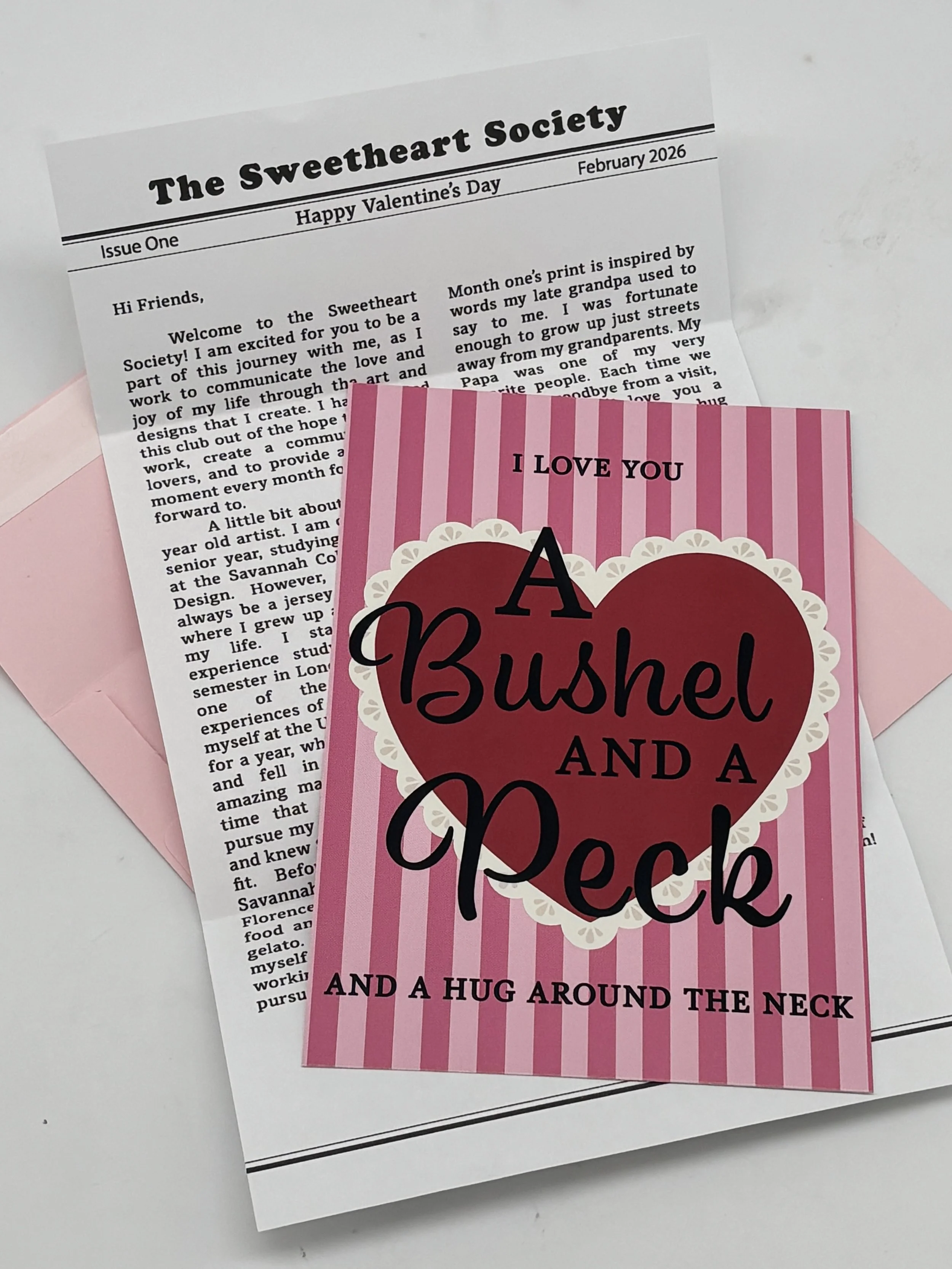 Valentine's Day card with pink and red stripes and a heart shape, reading 'I love you. A bushel and a peck and a hug around the neck.' Behind the card is a letter with the heading 'The Sweetheart Society.'