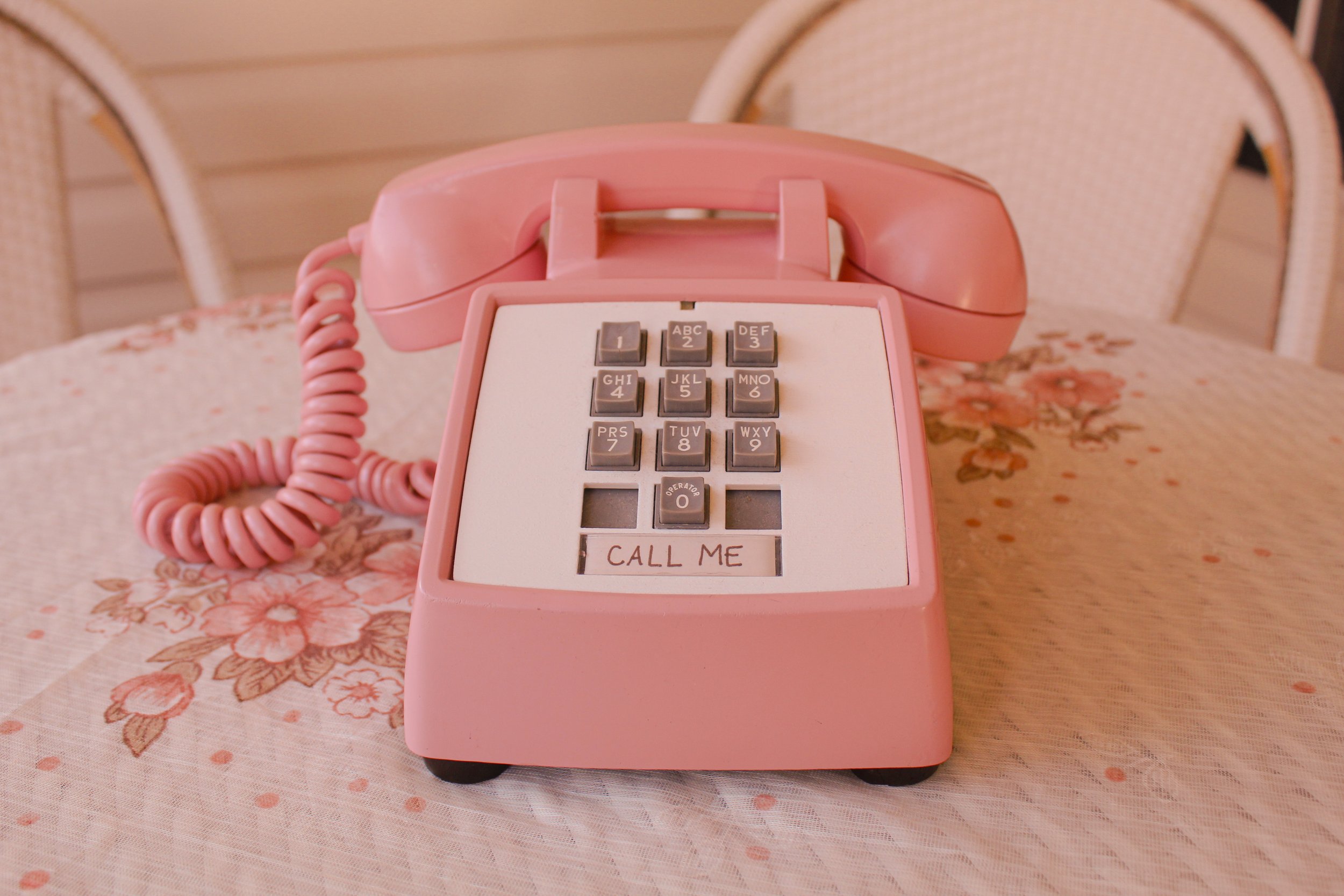 Pink vintage rotary landline telephone on a floral tablecloth.