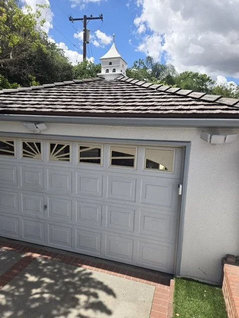 Close-up view of residential gray asphalt shingle roof with white paneled garage door visible below.,