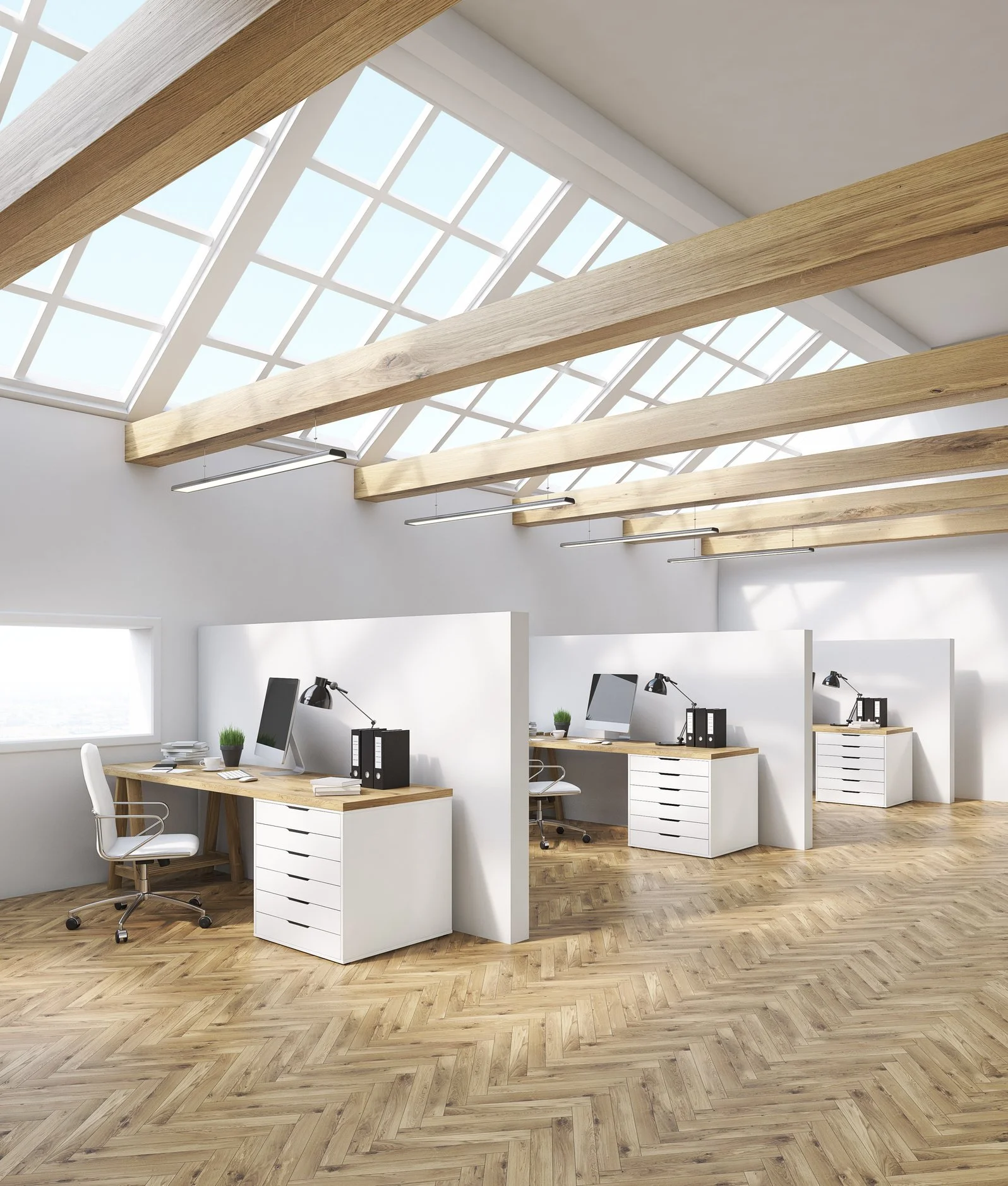 Modern office space with three workstations separated by white partitions, each with a computer, desk lamp, and office chair, under a slanted glass ceiling with wooden beams.