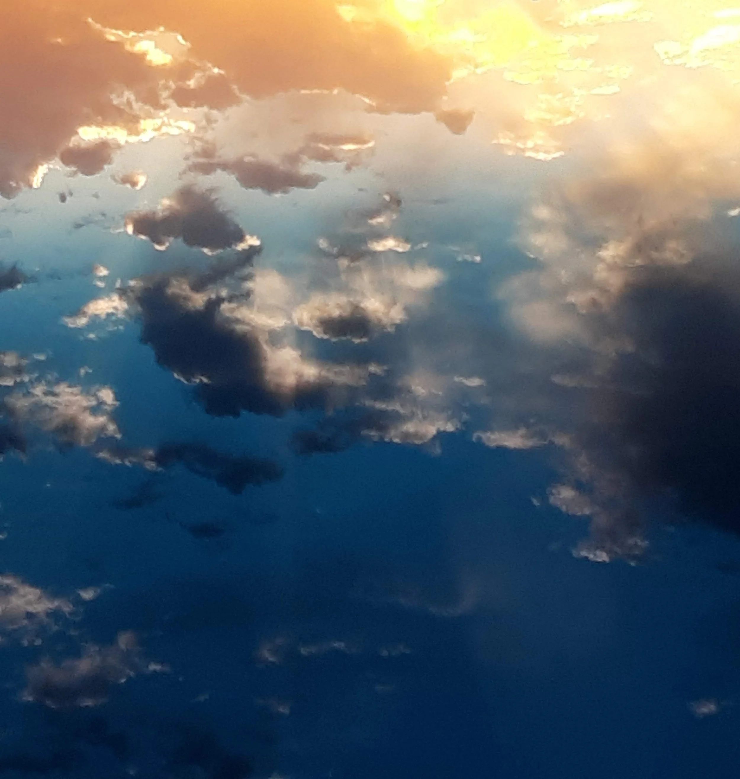 Cloudy sky during sunset or sunrise with golden and dark gray clouds reflecting on the water surface.