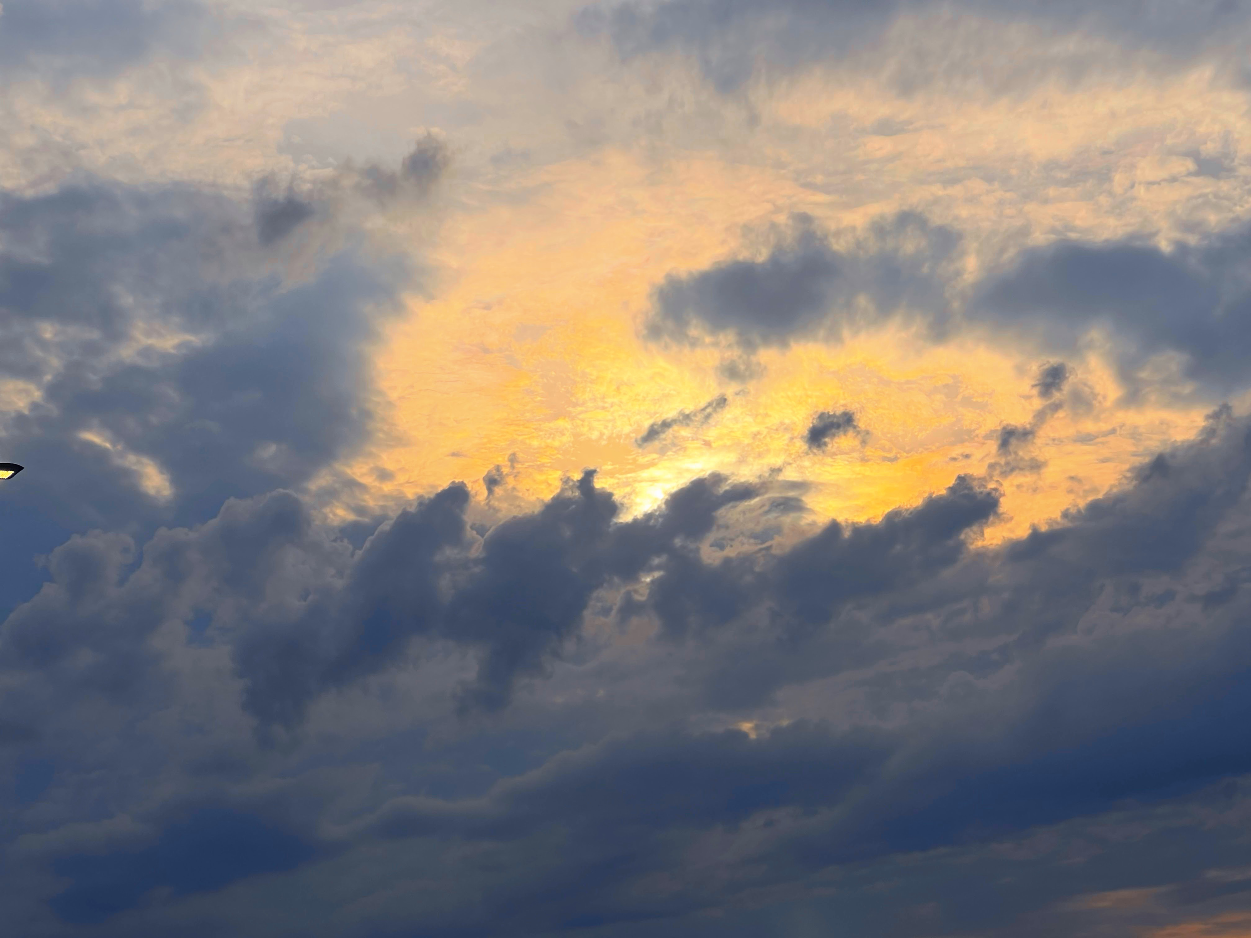 Cloudy sky with the sun partially visible and casting a yellow glow through the gaps in the clouds.