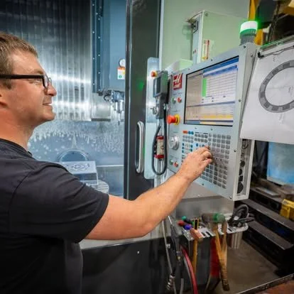 A man working on a CNC machine in a manufacturing facility.