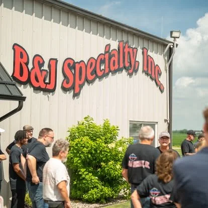 People standing outside B&J Specialty Inc. building with a large shrub in front of it.