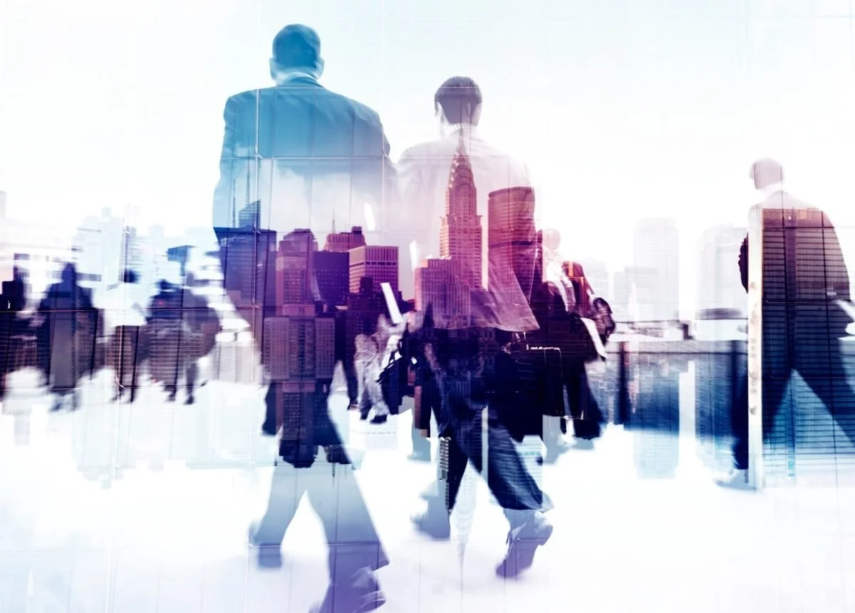 Silhouettes of business people walking in a cityscape with tall buildings, overlaid with a double exposure of a city skyline.