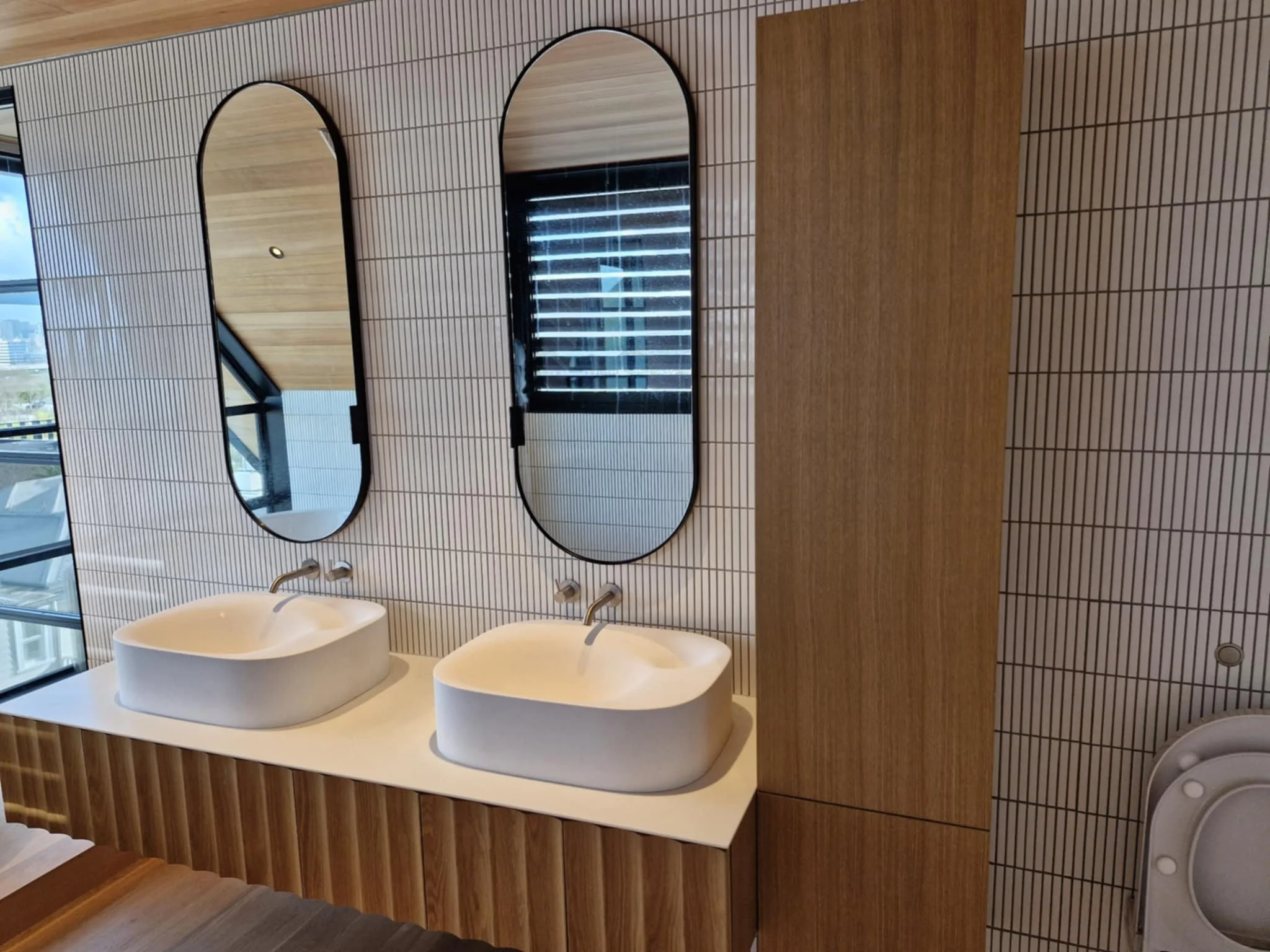 Modern bathroom with white vanity, rectangular sink, large mirror, hanging pendant lights, and a bathtub in the background.