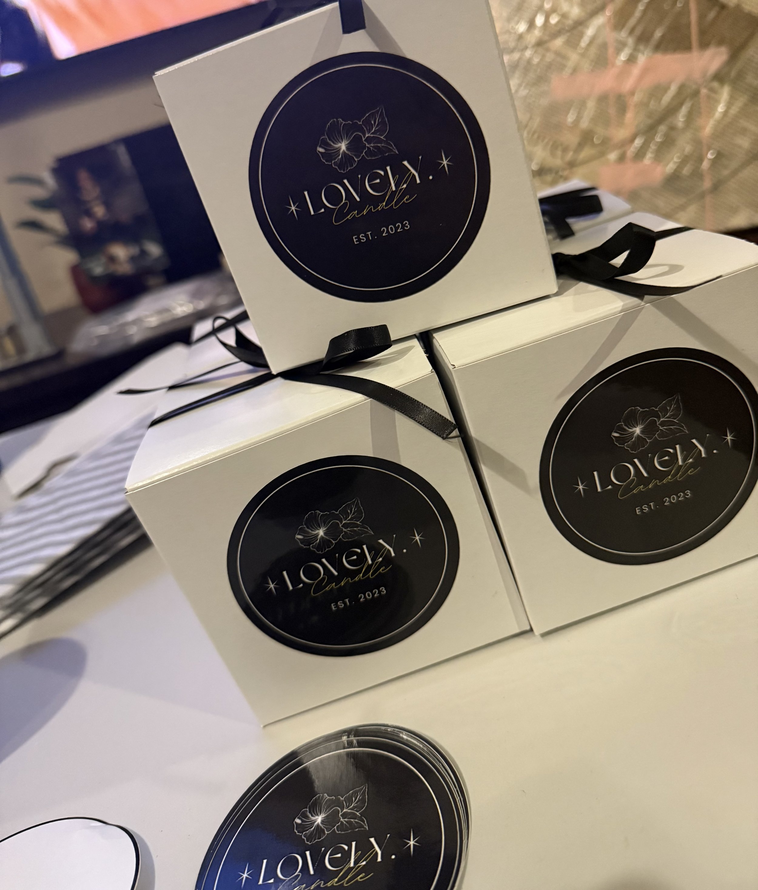 Boxes of 'Lovely Candle' with black labels featuring a floral design and the text 'Est. 2023'.