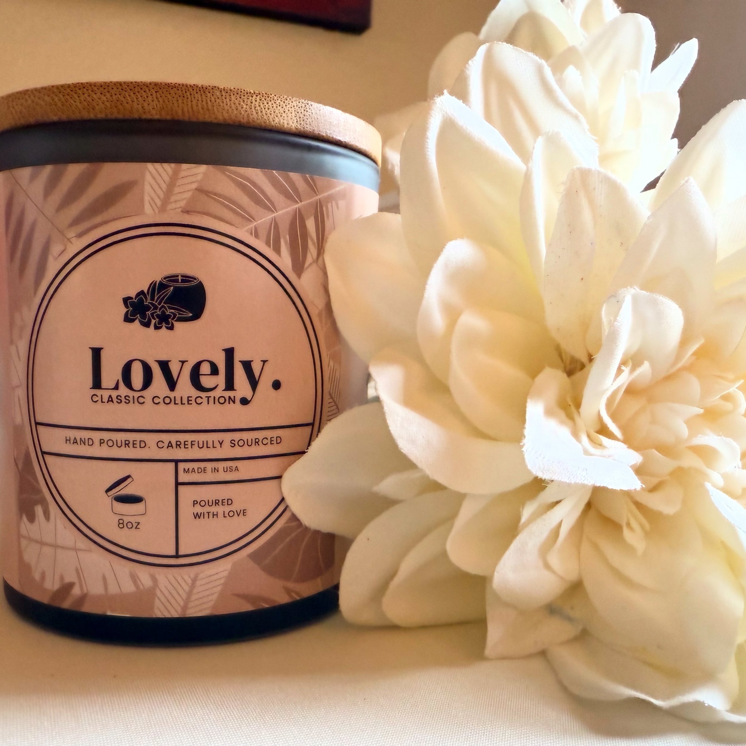 A candle labeled 'Lovely Classic Collection' with a wooden lid and a cream-colored flower beside it.
