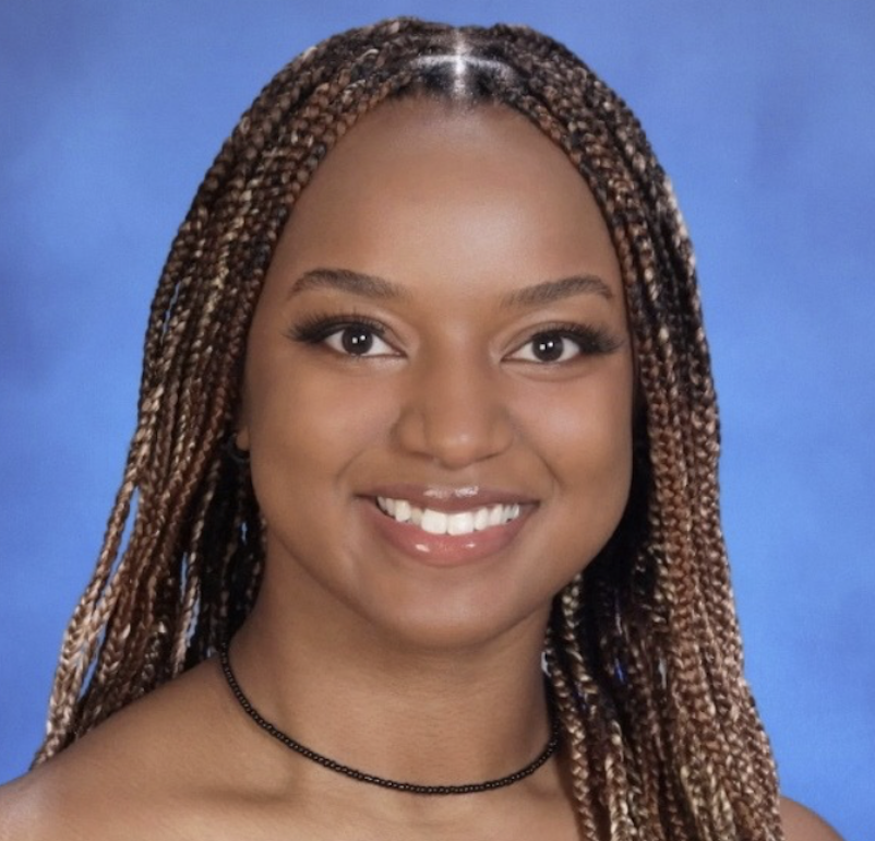 A young woman with braided hair and a bright smile posing for a portrait against a blue background.