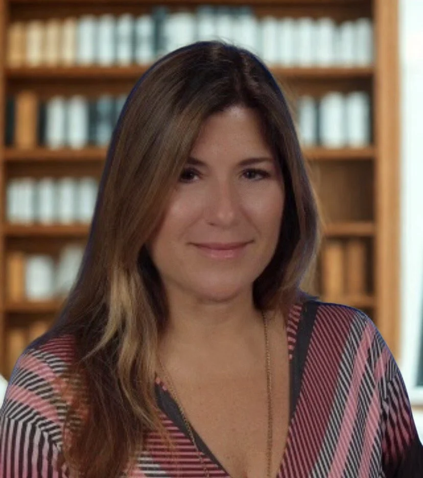 A woman with long, wavy brown hair smiling against a blue background, wearing a striped multi-colored top.