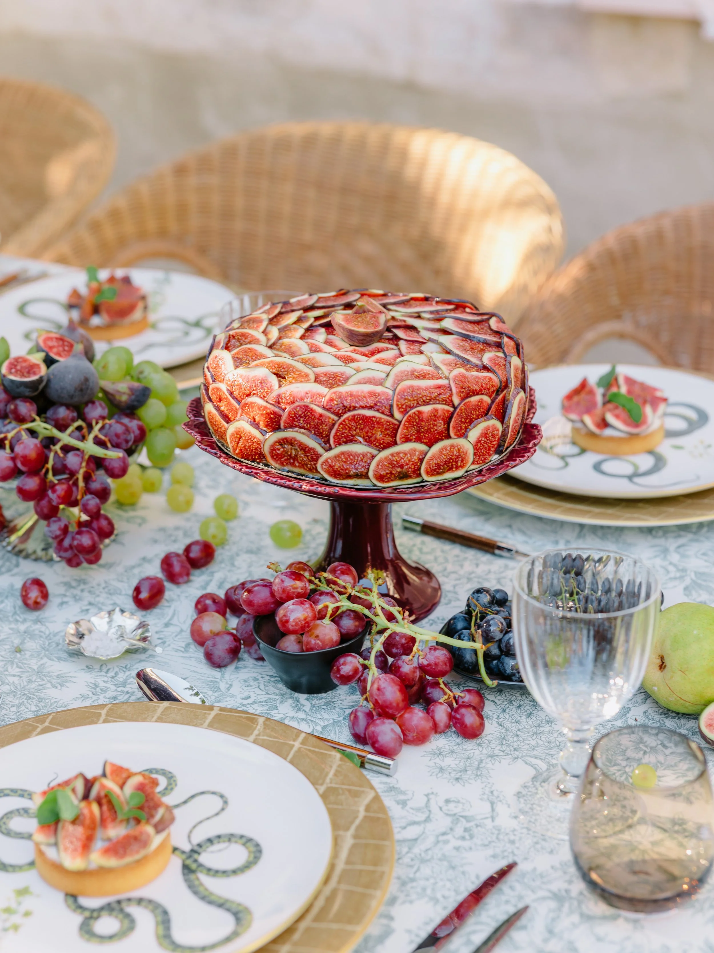 Table set with grapes, figs, and a decorated cake with fig slices on top.