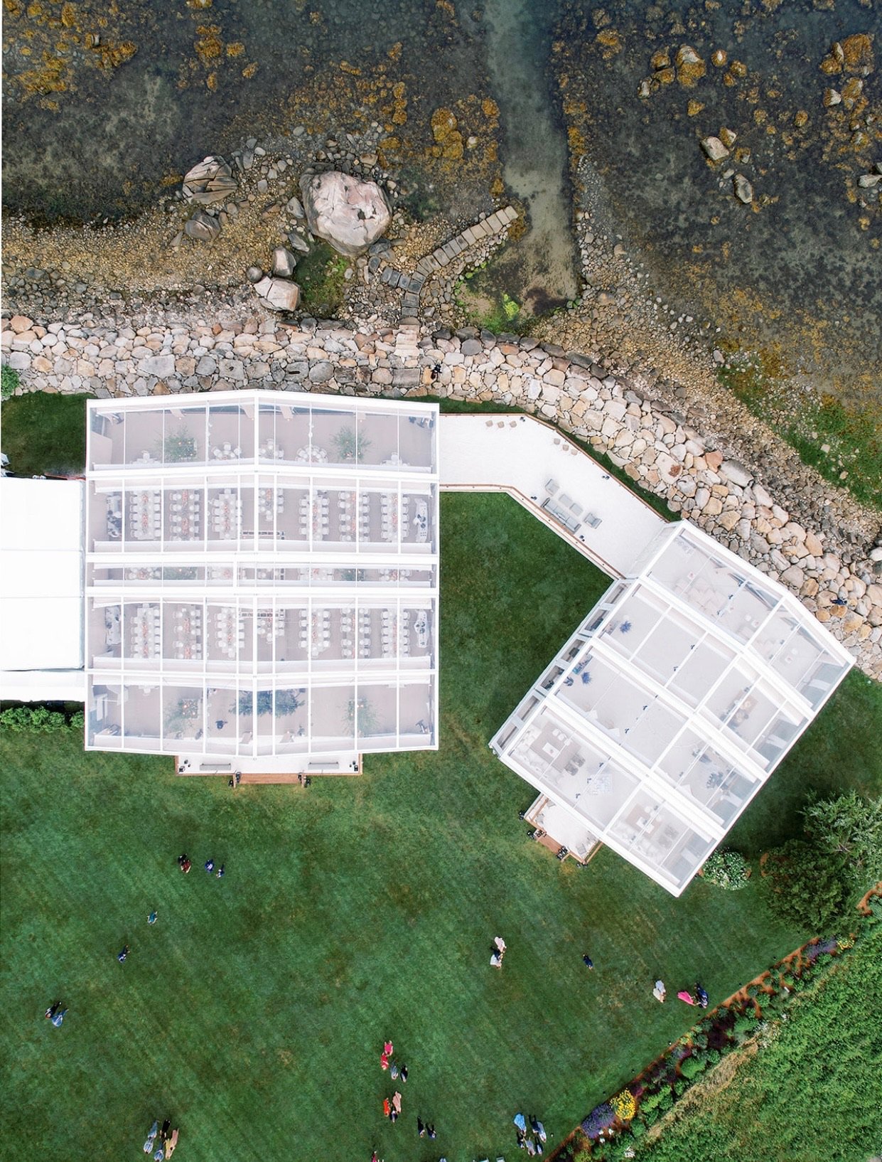 Aerial view of two modern glass buildings with green lawn, people walking, rocks, and rocky terrain.