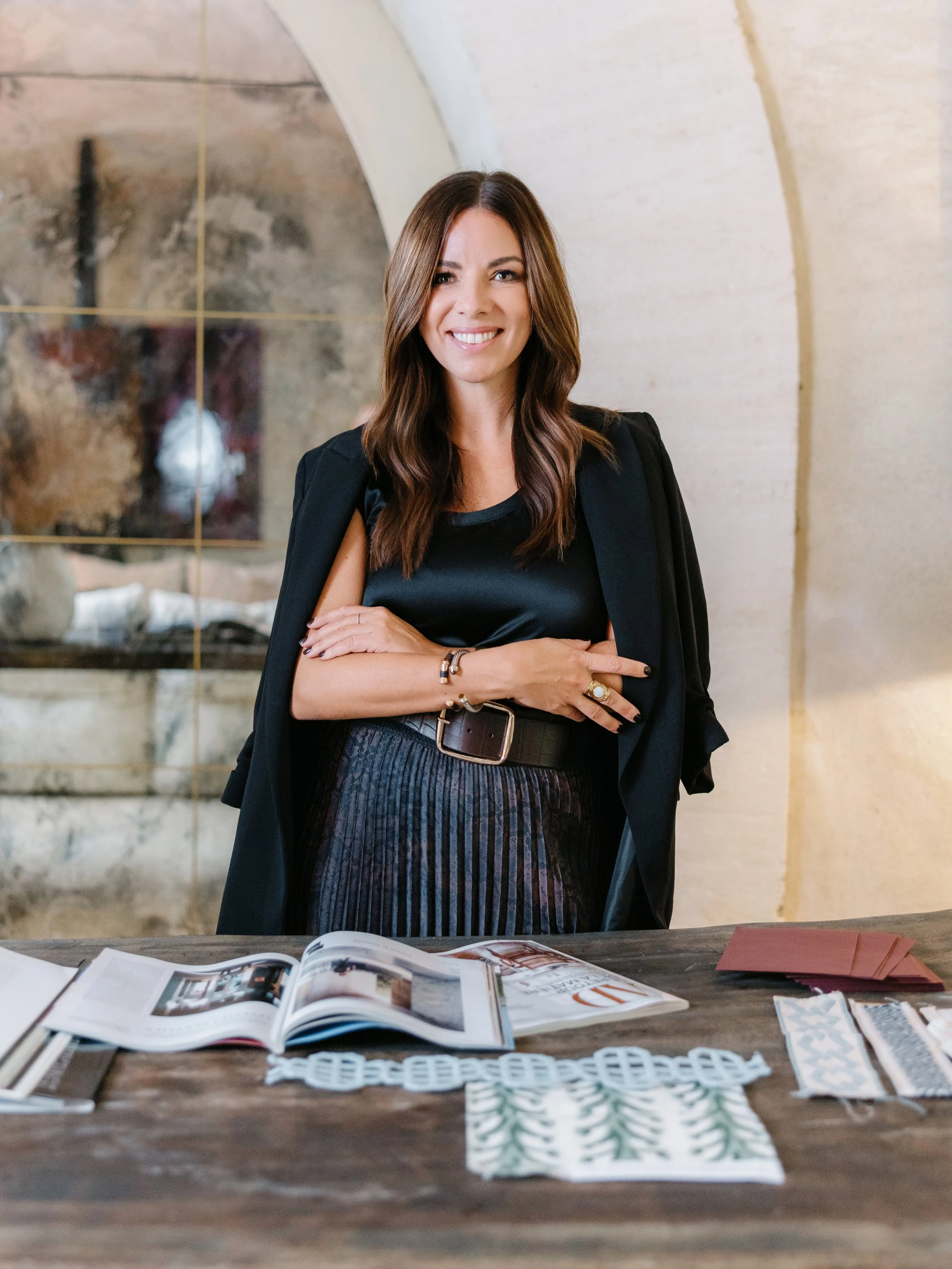 A woman with long brown hair smiling and standing behind a table with magazines and fabric samples.