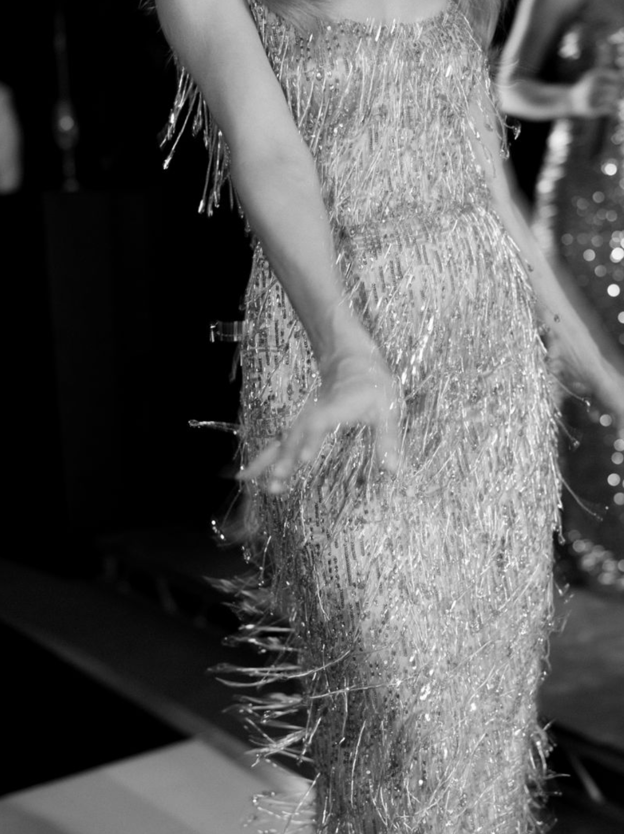 Close-up of a dress with numerous shiny fringe details, likely at a fashion event or runway show.